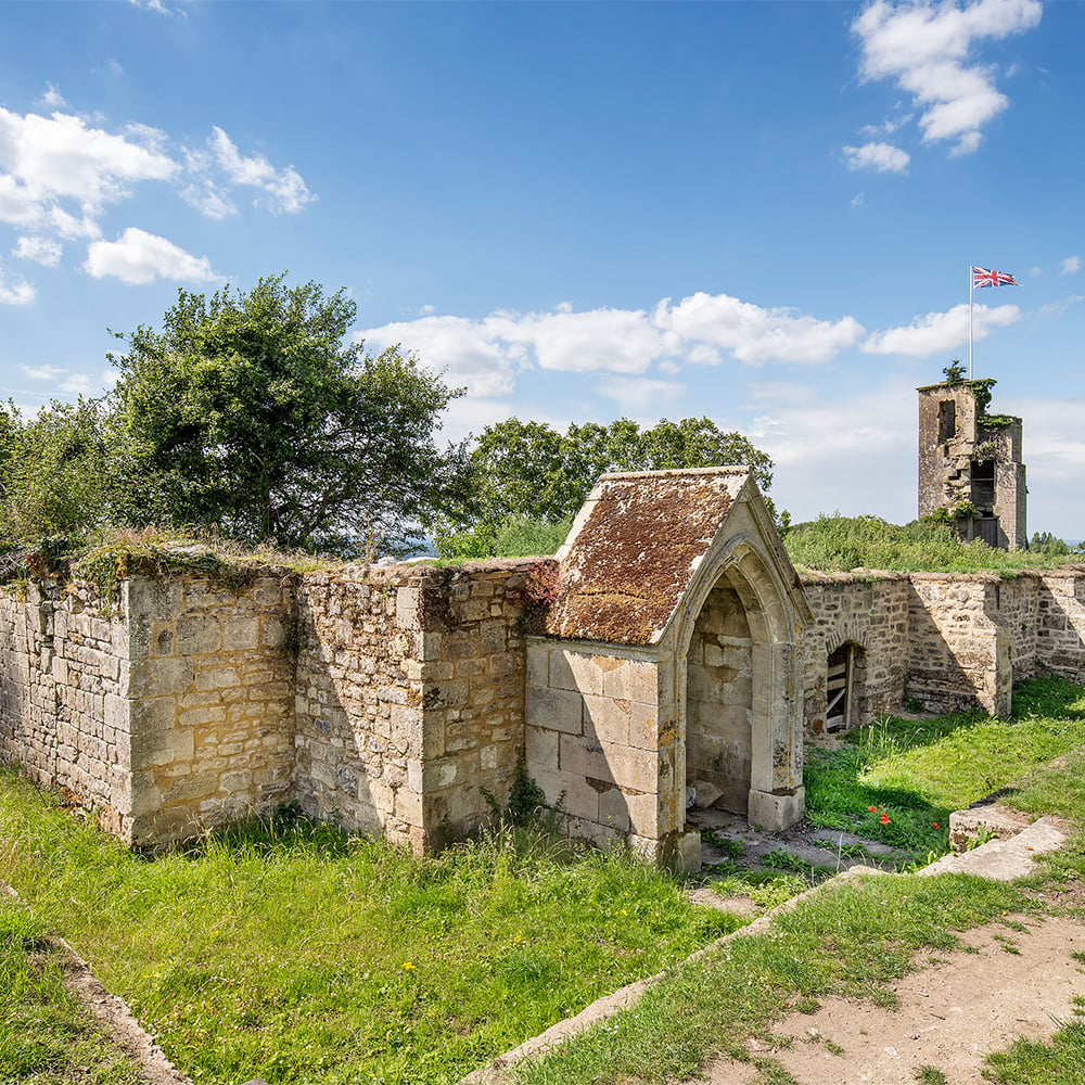 A general view of a stone priory ruins, flying a union jack flag in the background from a tower, or higher part of the priory. 