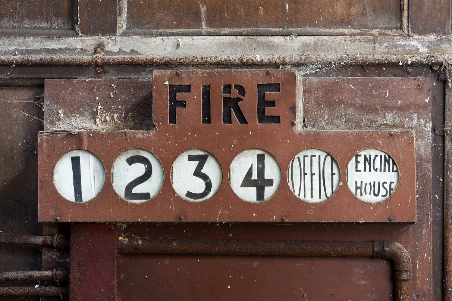 An old, red alarm panel attached to a wall. Underneath the word FIRE are indicators reading 1, 2, 3, 4, Office, Engine House.