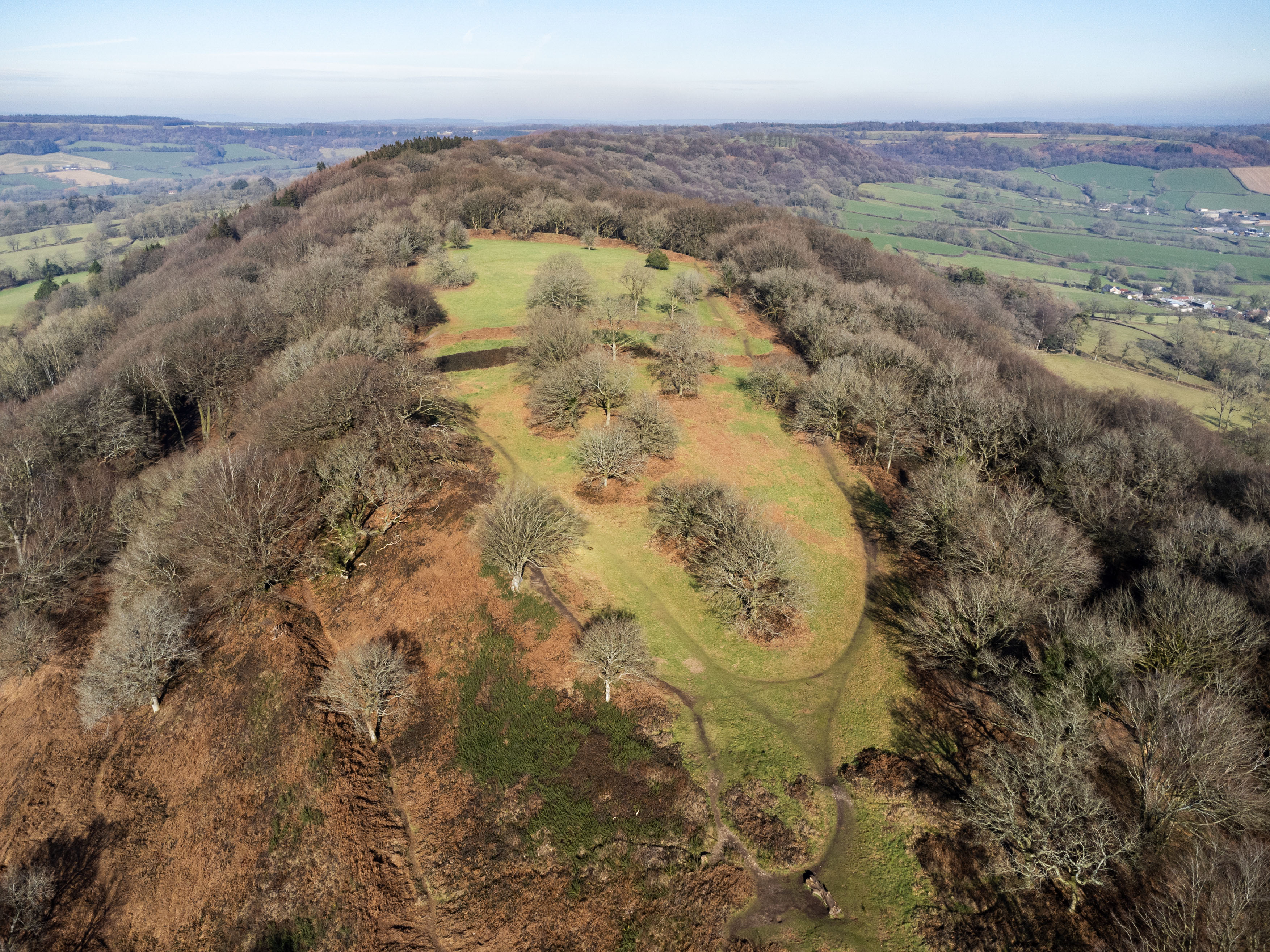 An aerial photograph showing a view over a landscape with a large promontory in the foreground. It has archaeological features on it, forming an oval-shaped enclosure.