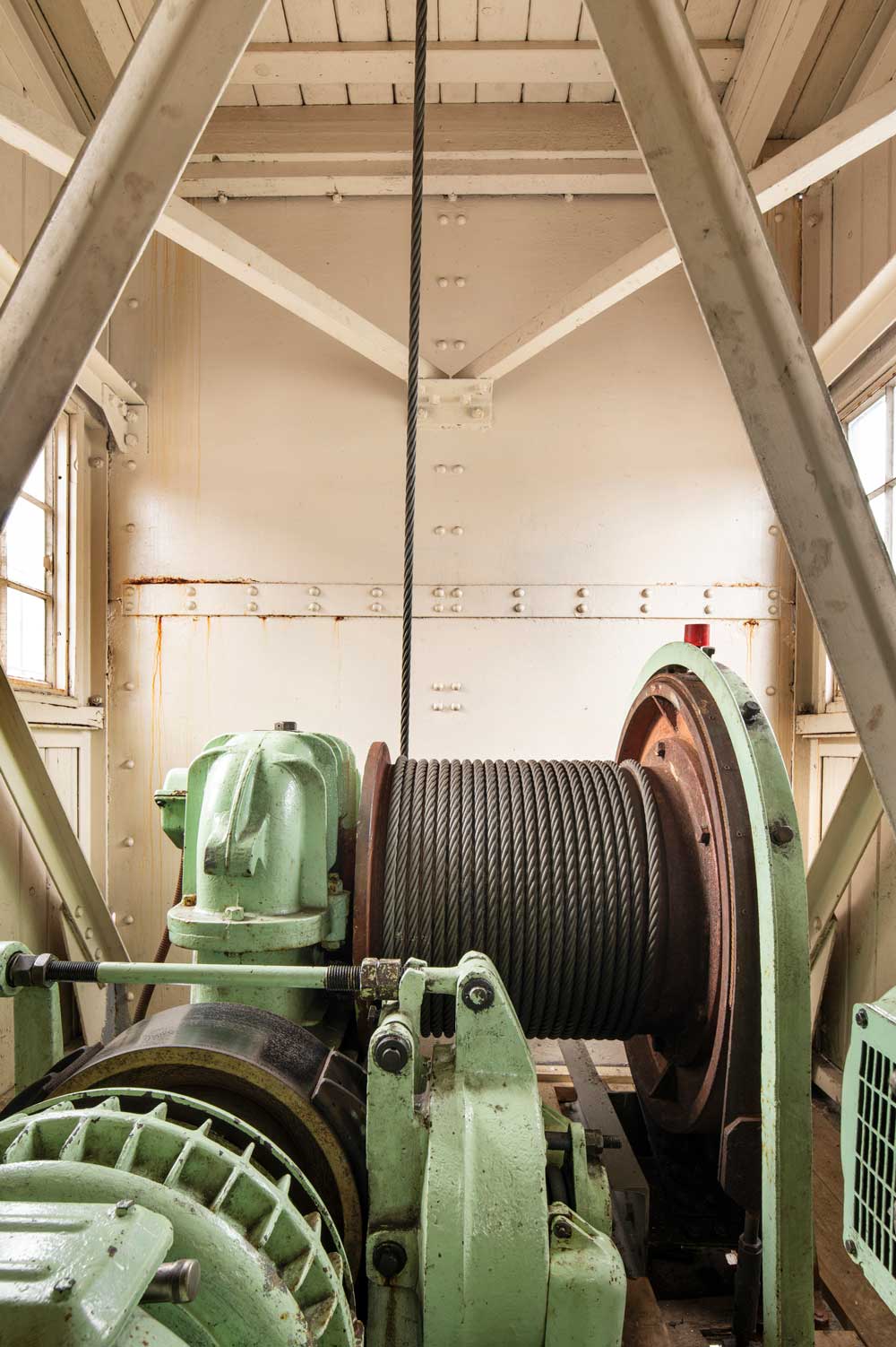 A photograph of the inside of a crane's motor room showing a large cable winch.
