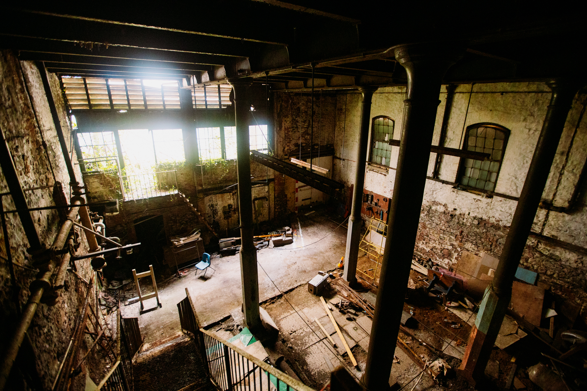A photograph of a large, interior space in a poor state of repair. The ceiling is held up by tall, cast iron columns.