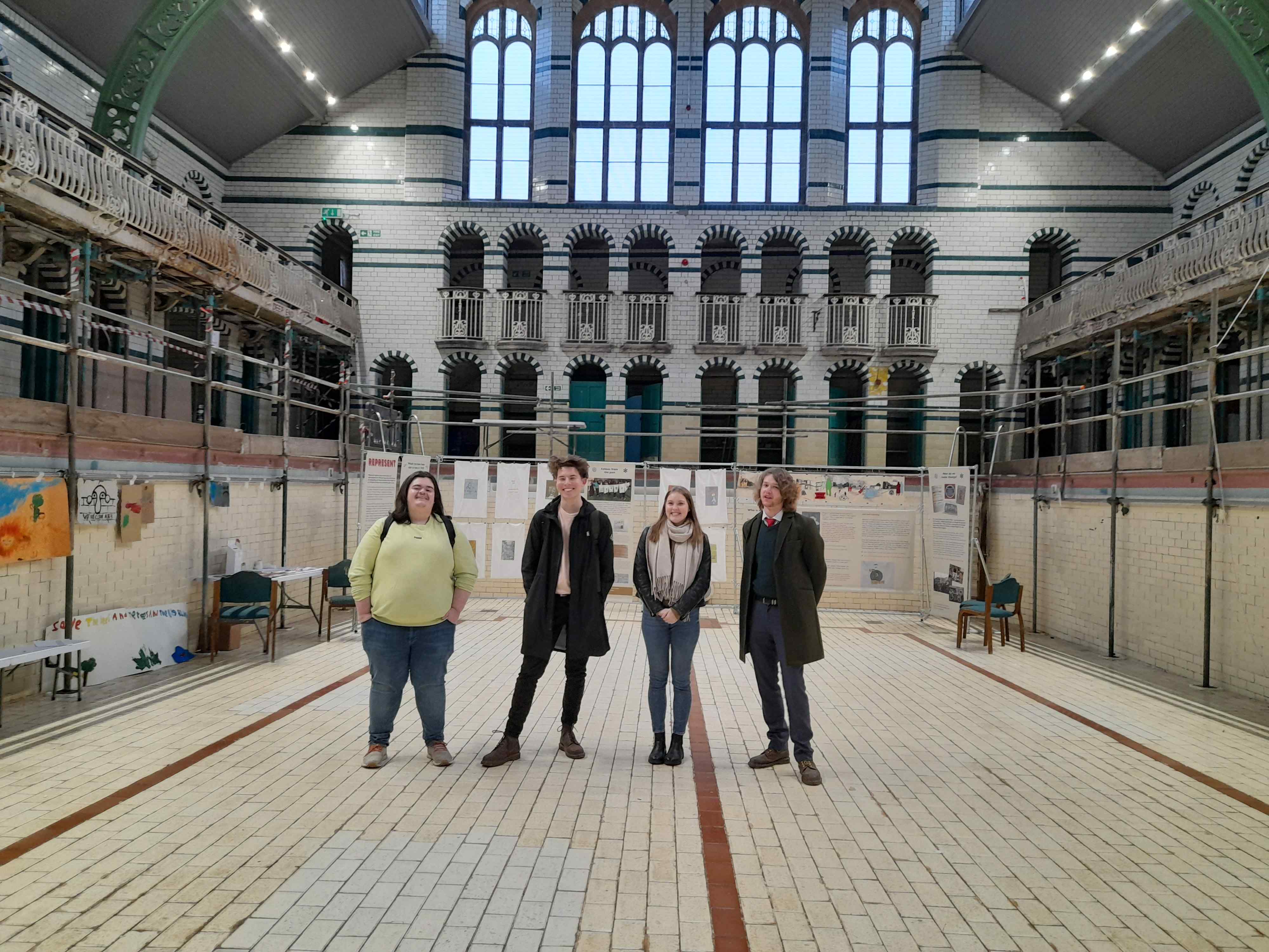A group of young people standing in the dry pool of a historic Victorian municipal baths building.