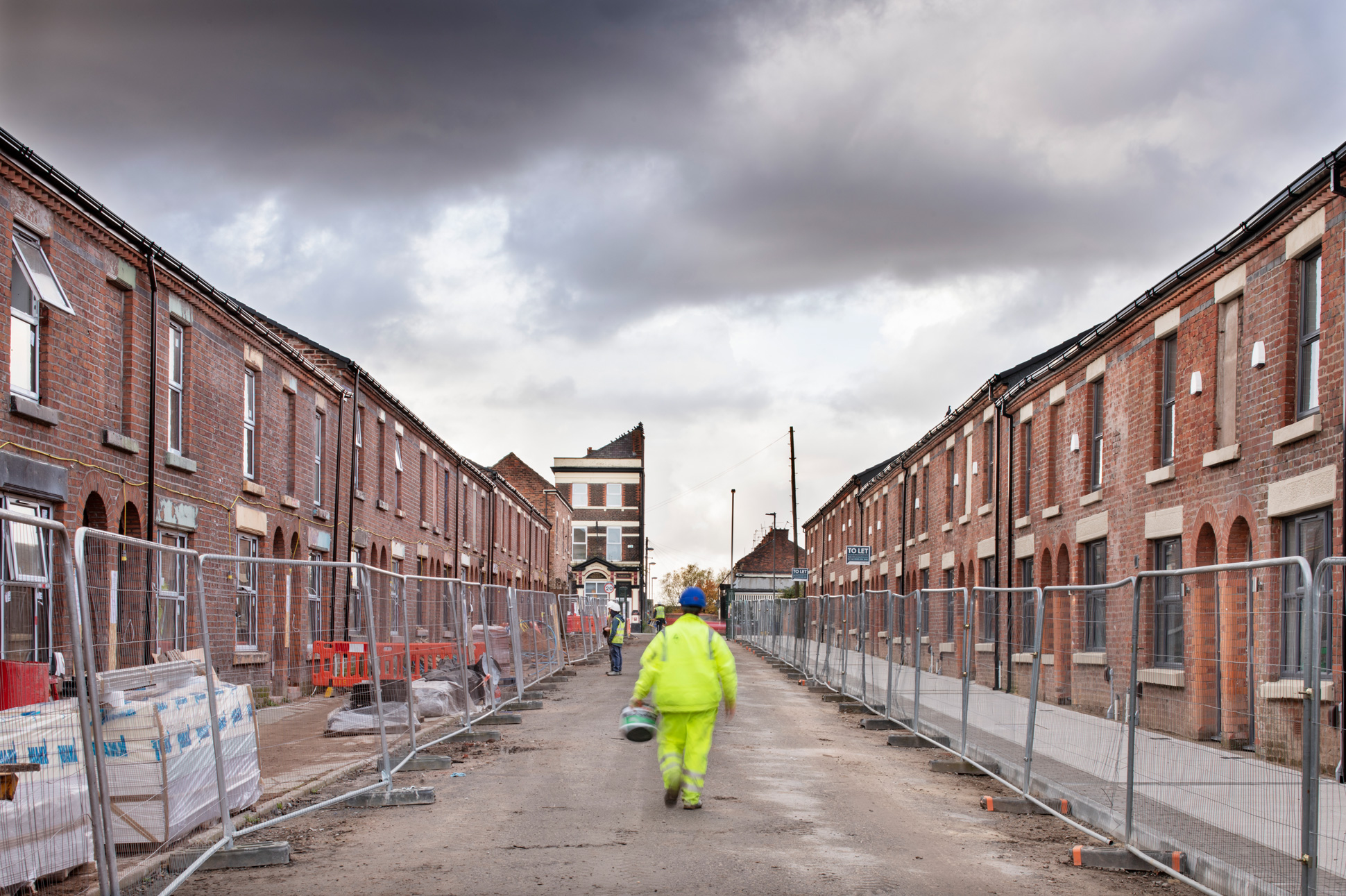 Street of terraced housing under building works with builders on site.