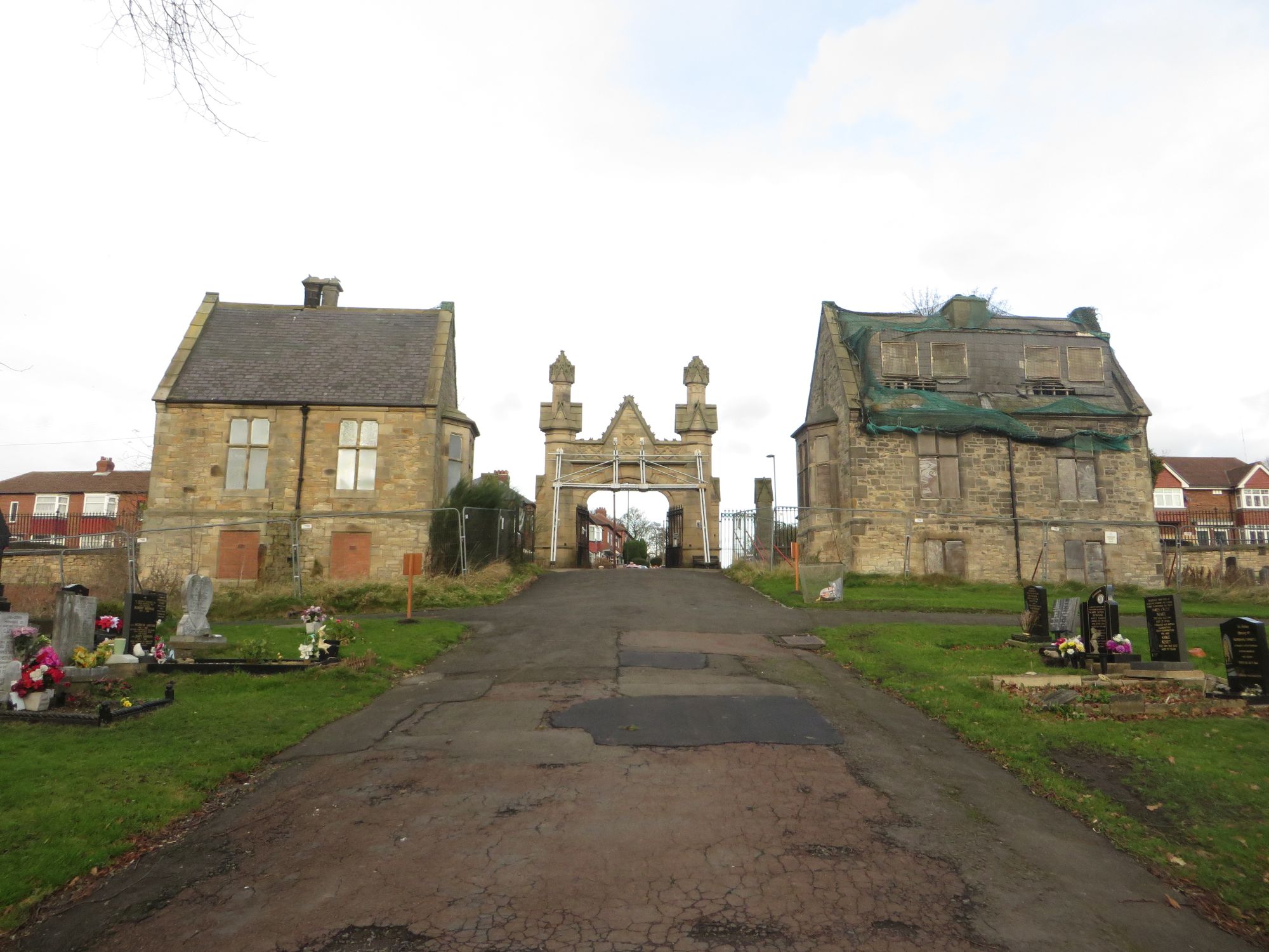 A gate flanked by two buildings in a cemetery. 