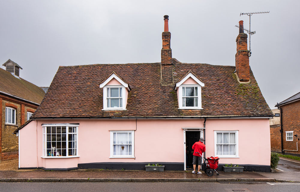 Pink cottage with postman and trolley standing at the front door.