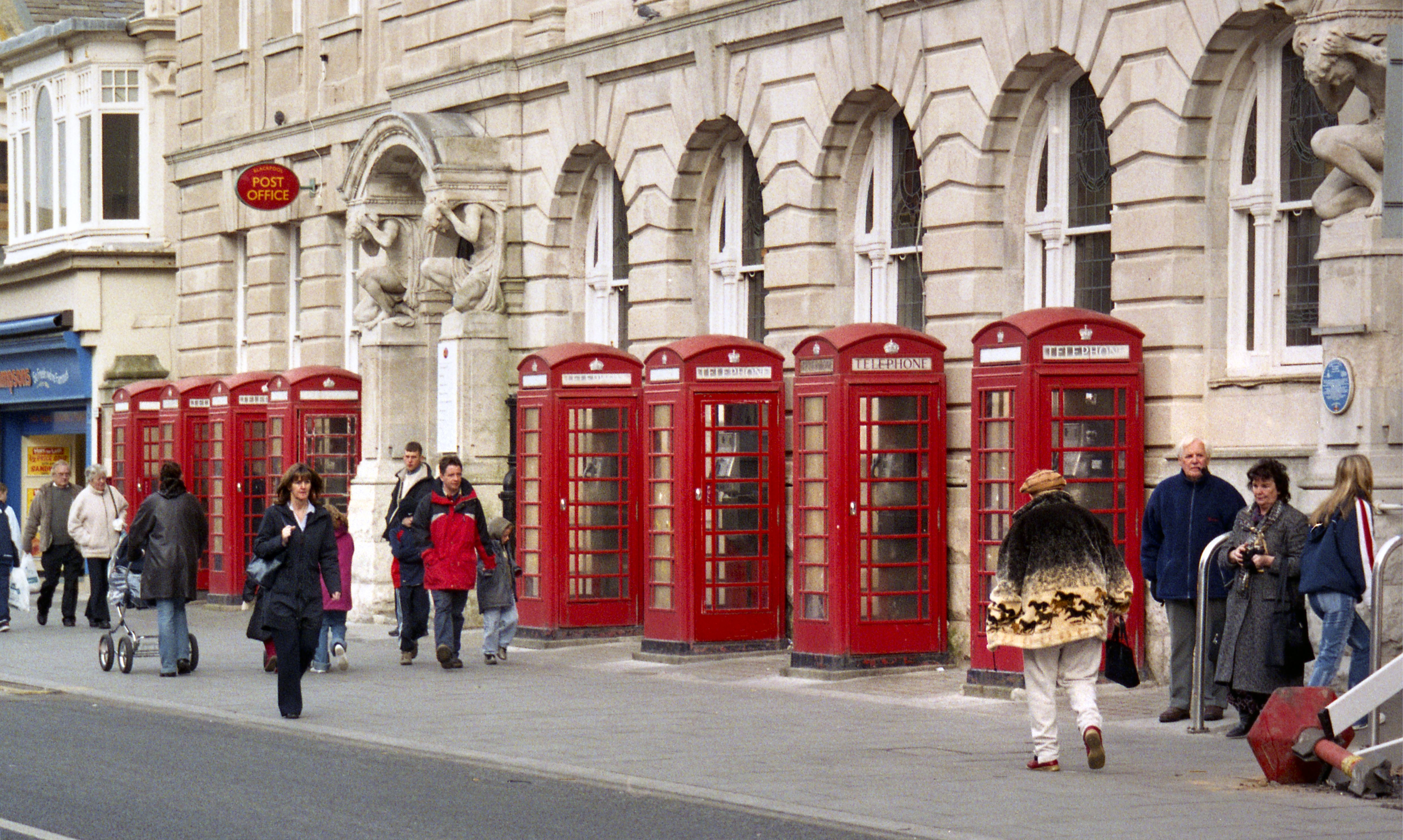 Group of eight K6 telephone kiosks with people walking past them