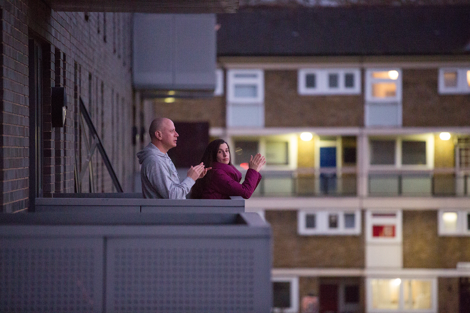 Man and woman standing on the balcony of a block of flats clapping their hands