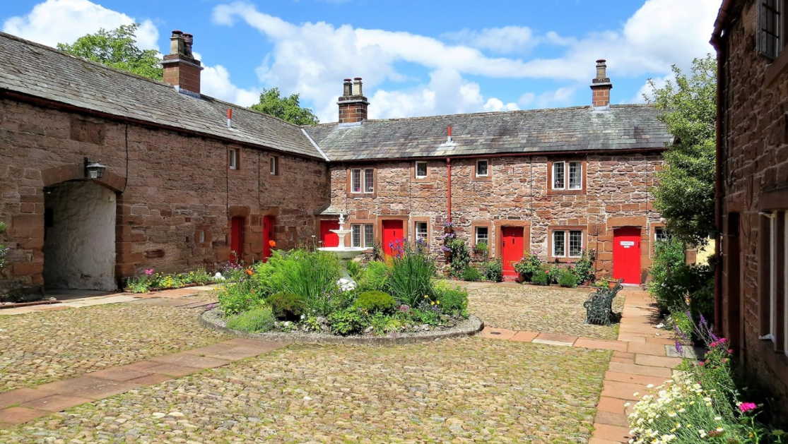 Almshouses built by Lady Anne Clifford for poor widows in Appleby. Stone cottages with red front doors around a courtyard with a fountain in the middle.