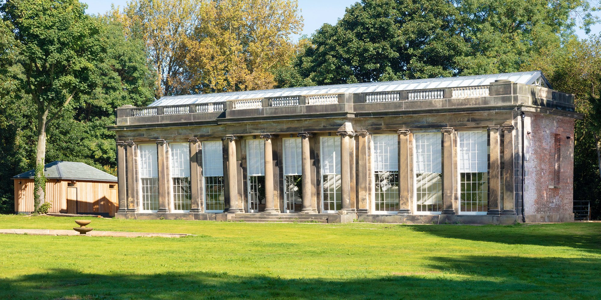 Exterior photo of a large formal botanical building with columns and tall windows. Lawns in front and trees beyond.