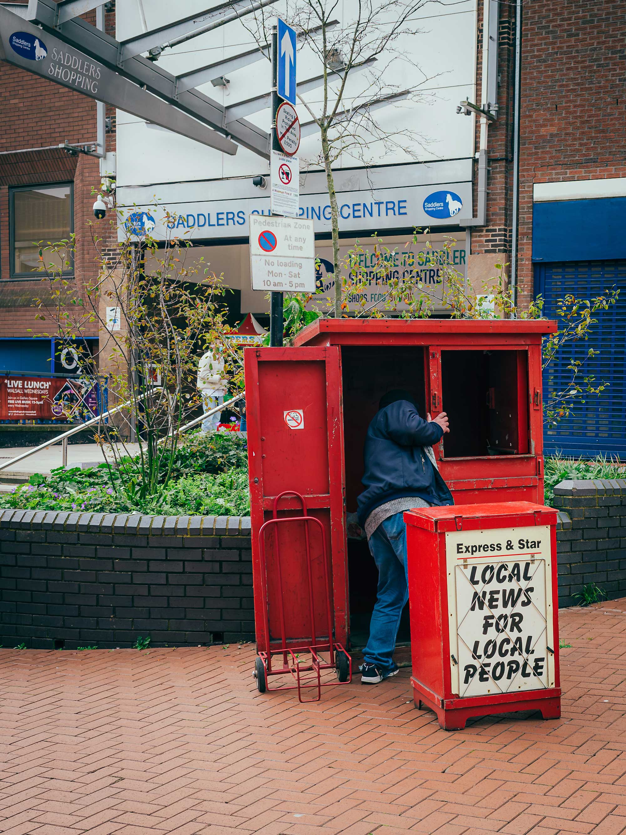 A person reaching into a newspaper street kiosk. The signage reads 'Express & Star. Local News For Local People'