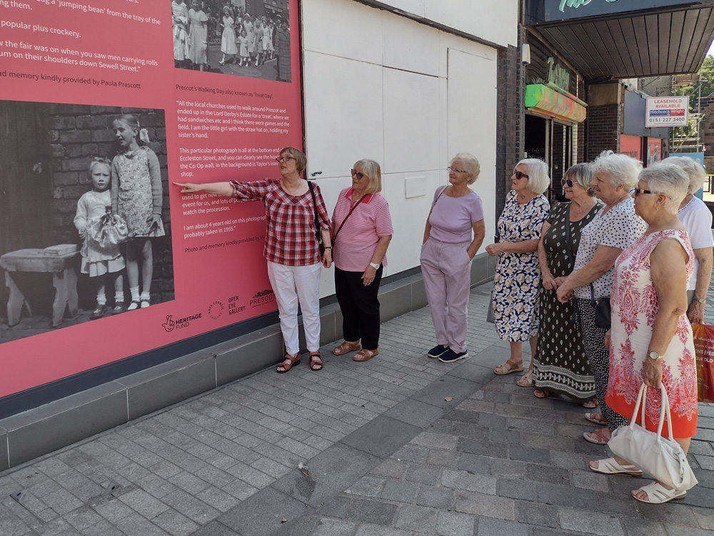 A group of women standing and observing a display of black and white photos and text.