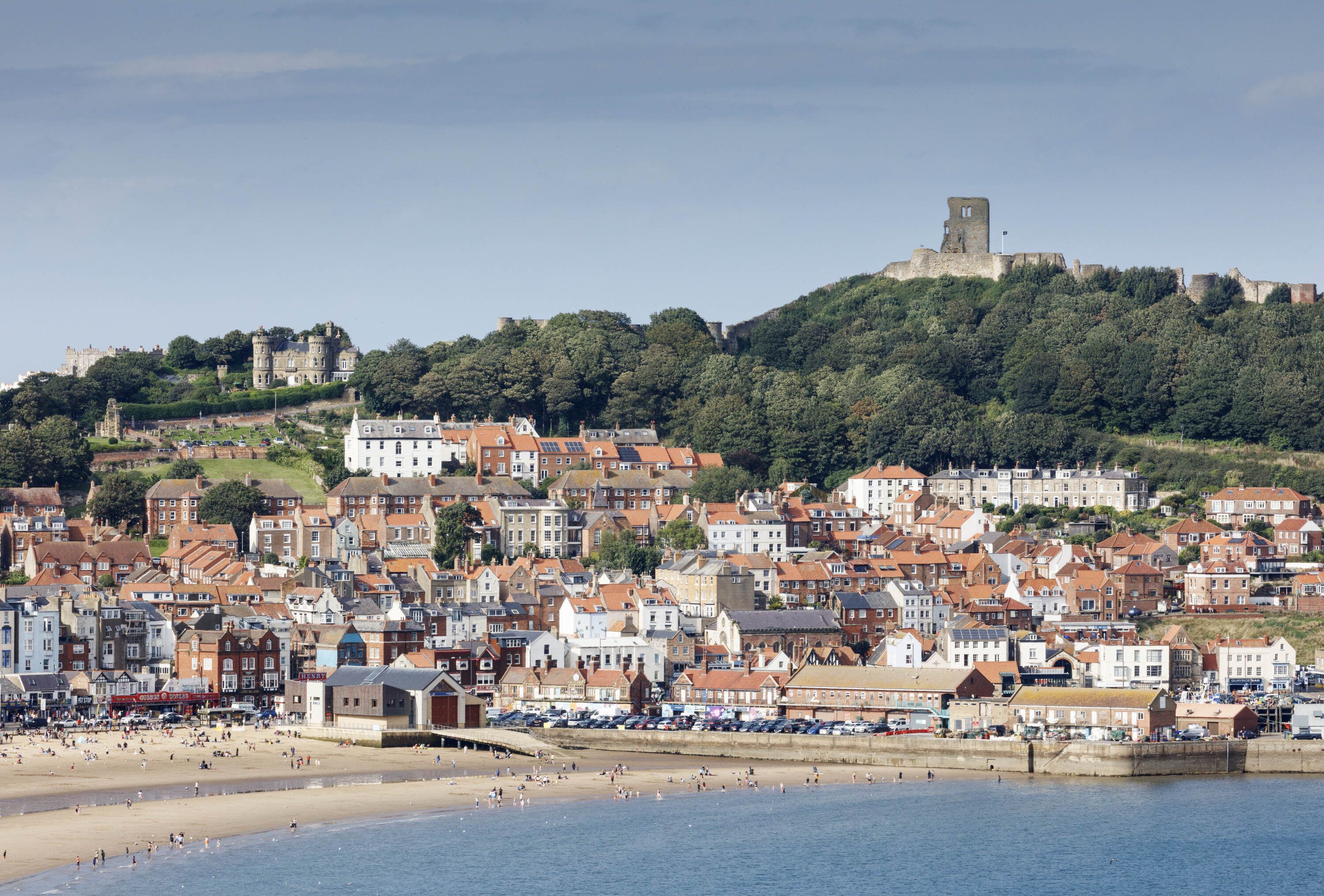 Daytime photo of the beach at Scarborough with a view of the gardens and castle above the bay. 