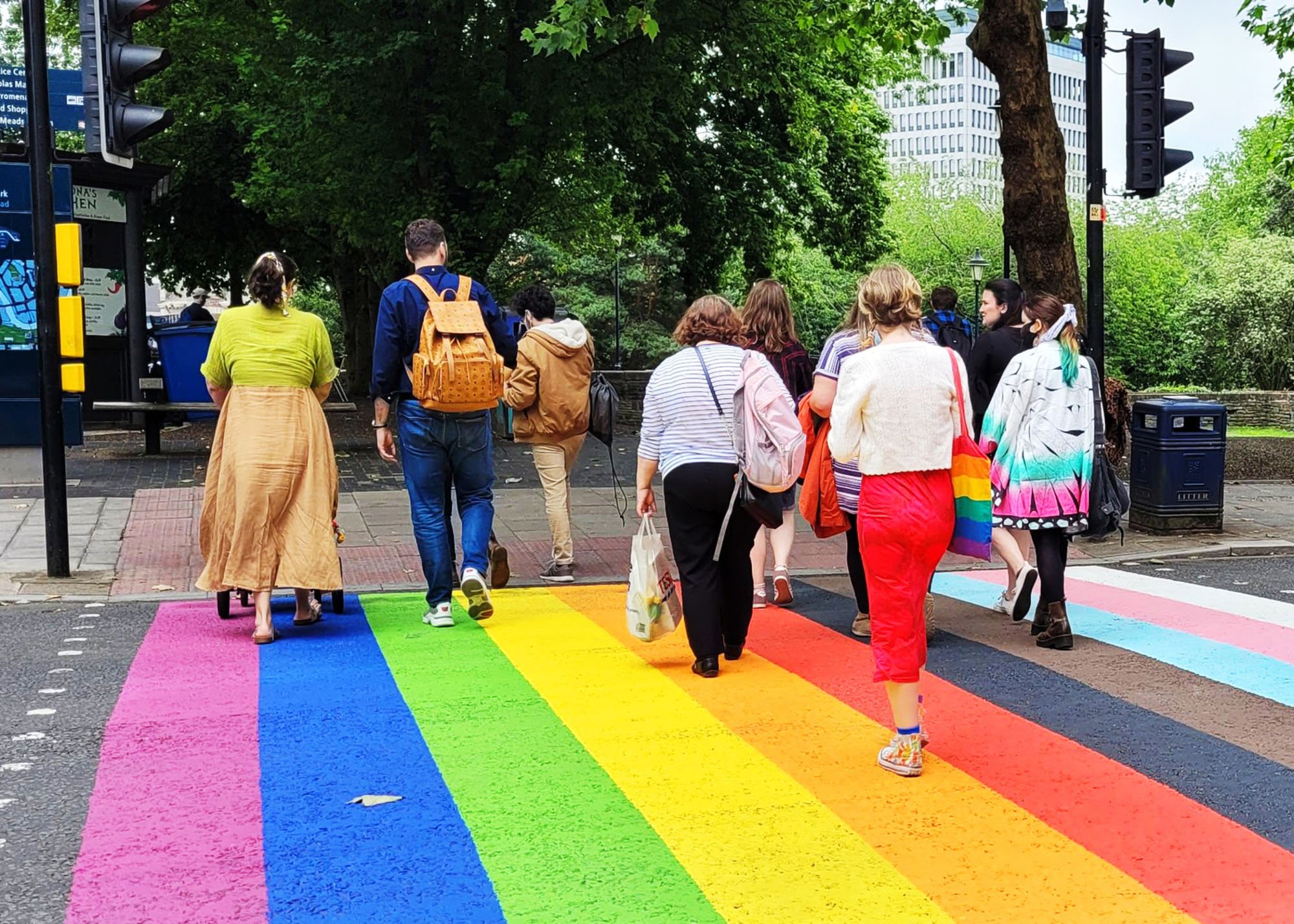 Pedestrians crossing a zebra crossing painted in rainbow colours.