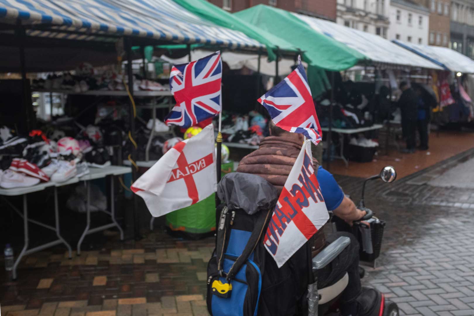A person in a mobility scooter, flying Union Jacks and England flags, driving passed market stalls.