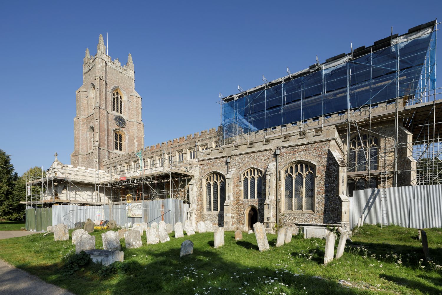 The side view of the church shows scaffolding at the right side of the church and a small graveyard in front of the church.