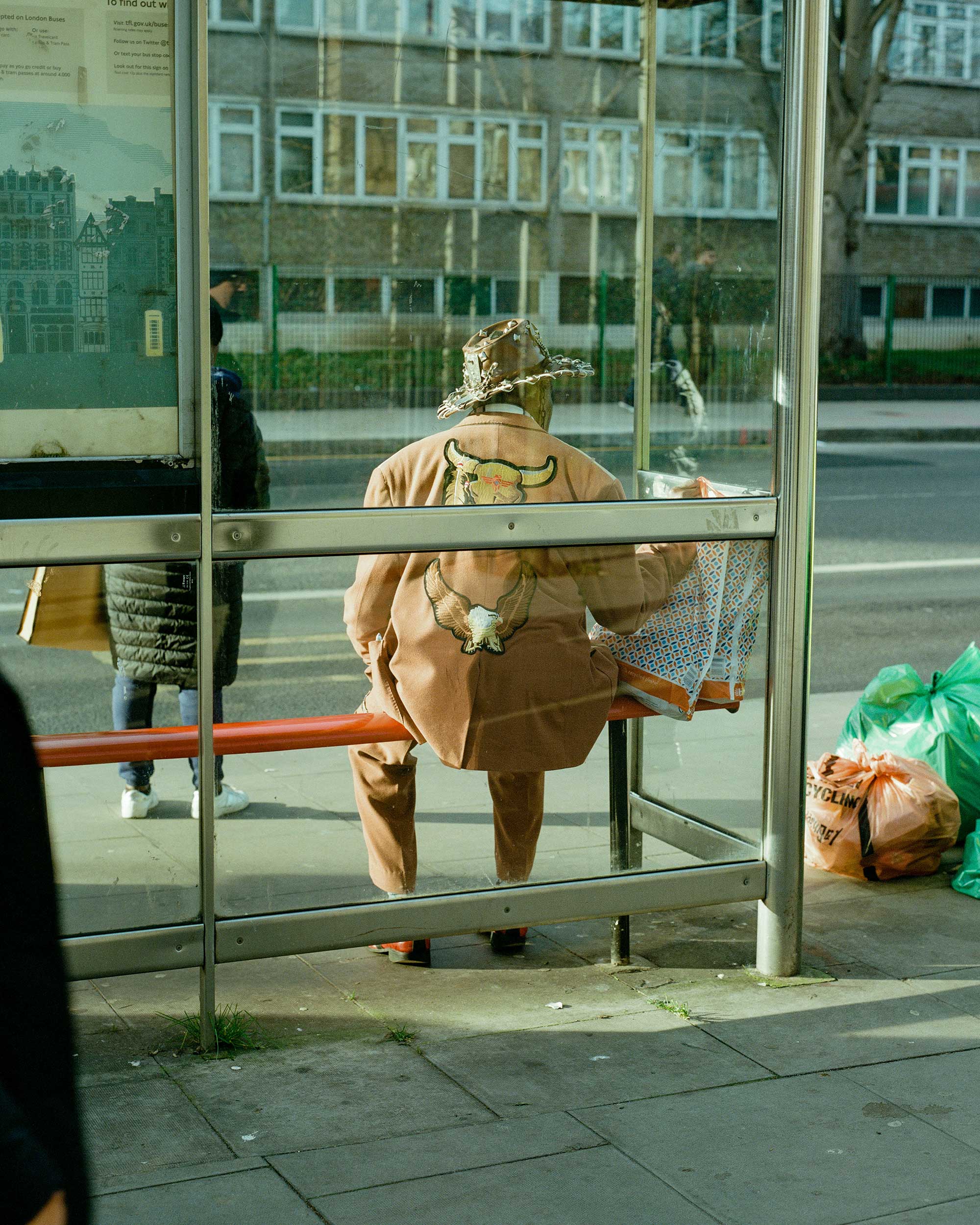 View of the back of a man sitting at a bus stop wearing a cowboy hat.
