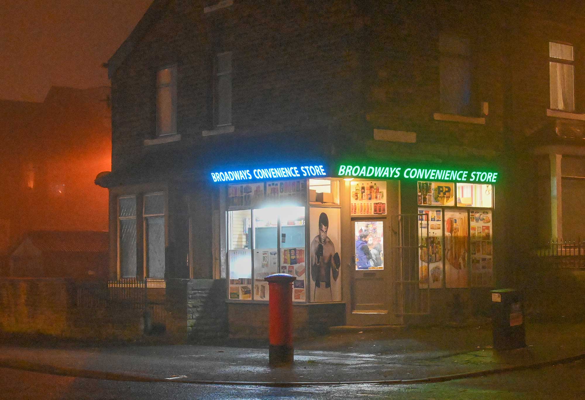 A night time scene showing the illuminated windows of the Broadways Convenience Store.