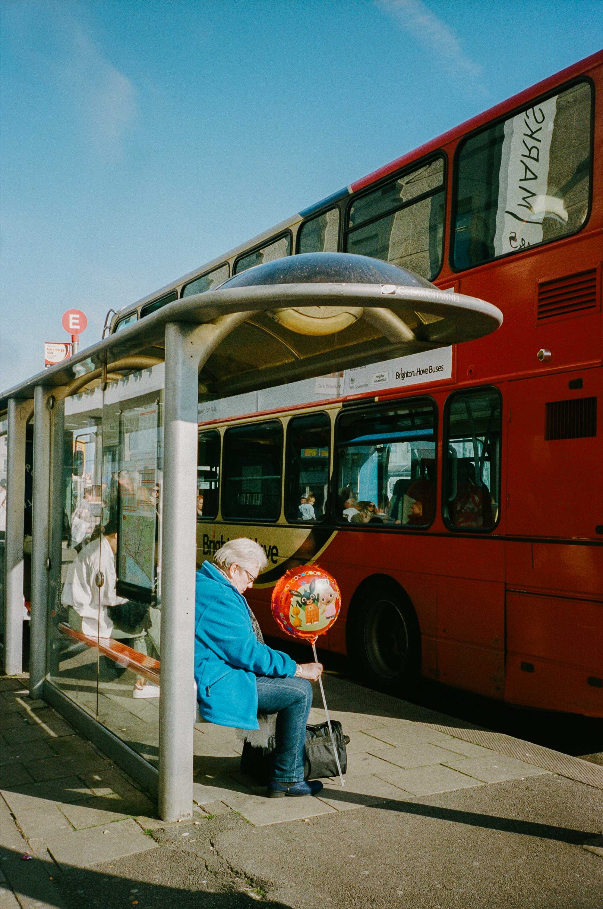 A woman sitting at a bus stop holding a balloon on a stick.