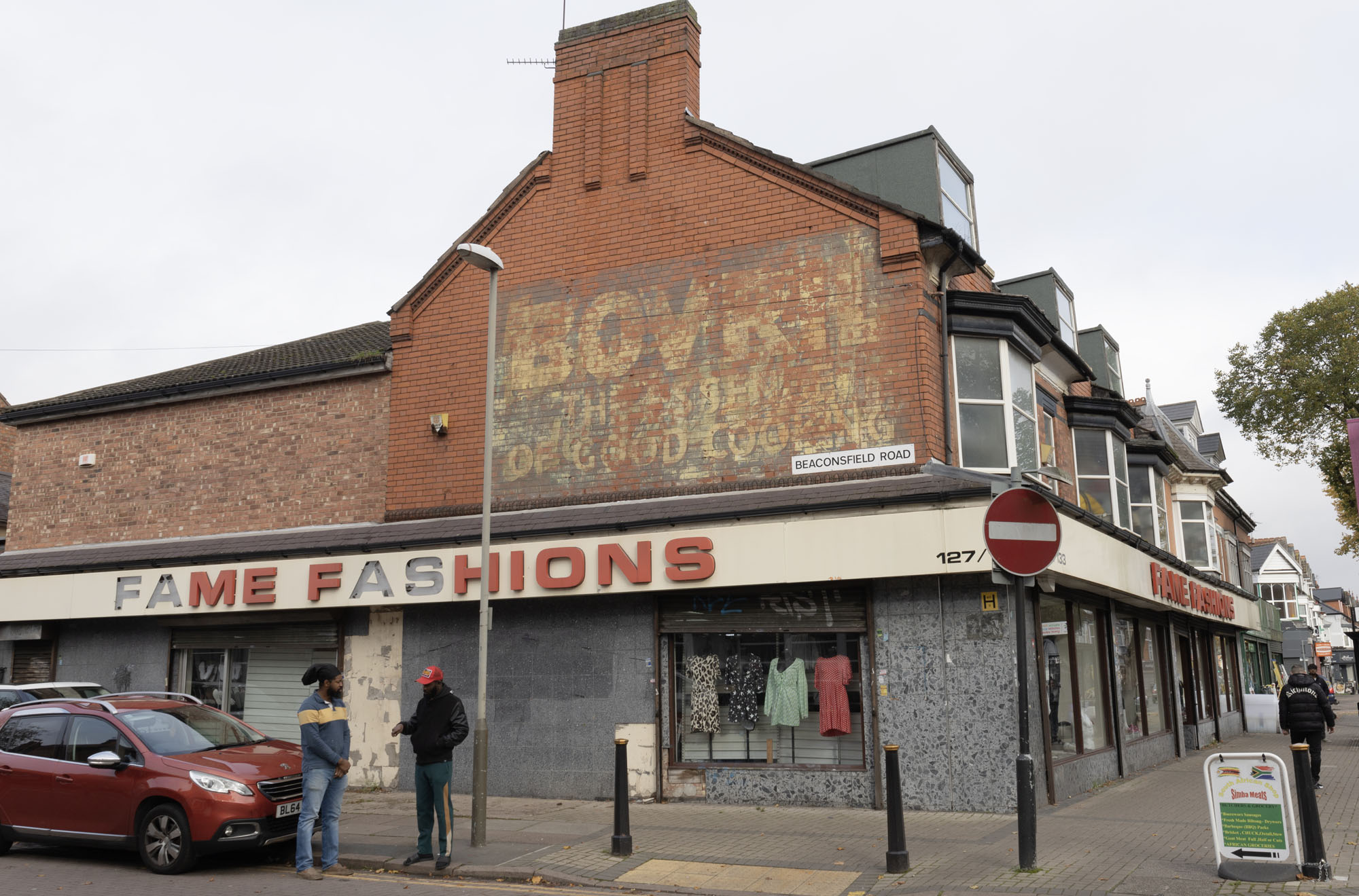 Ghost sign worded: 'Bovril - The Essence of Good Cooking' on the first floor of a building with another sign for current business 'Fame Fashions' beneath on the ground floor.