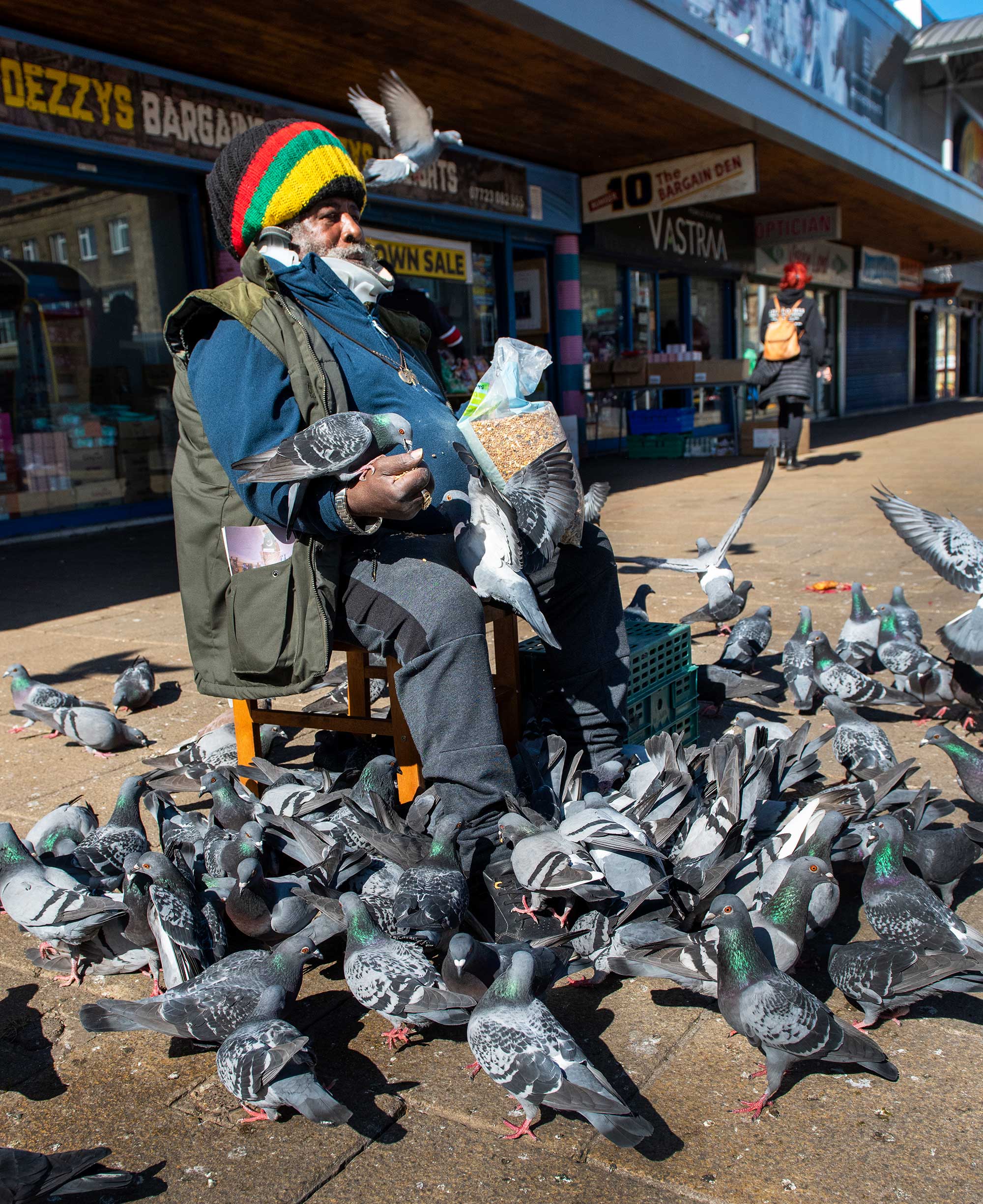 Portrait of a man sitting outside the Oastler Shopping Centre, feeding the pigeons.