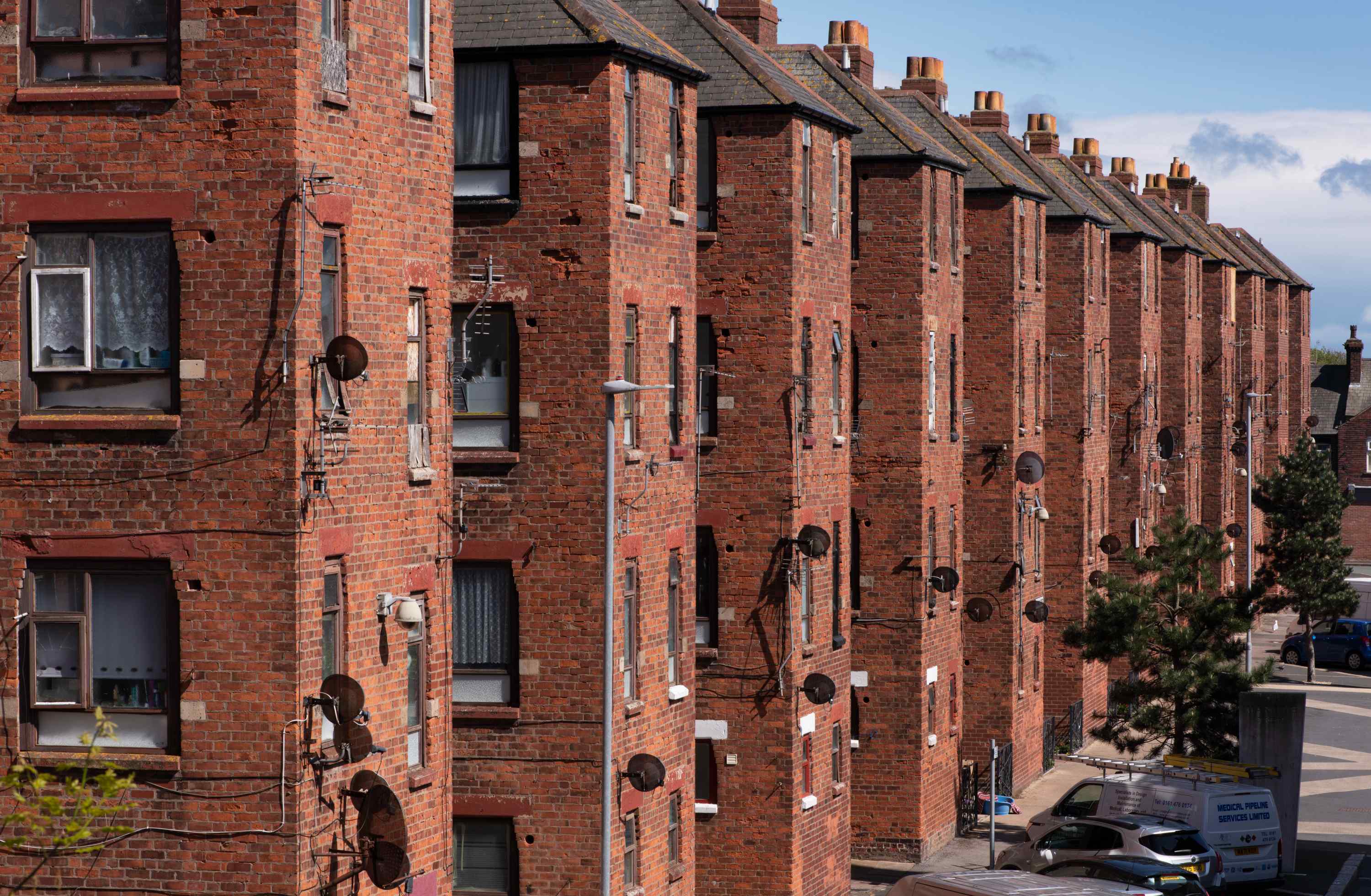 A photograph of a red brick tenement block building with numerous windows and satellite dishes