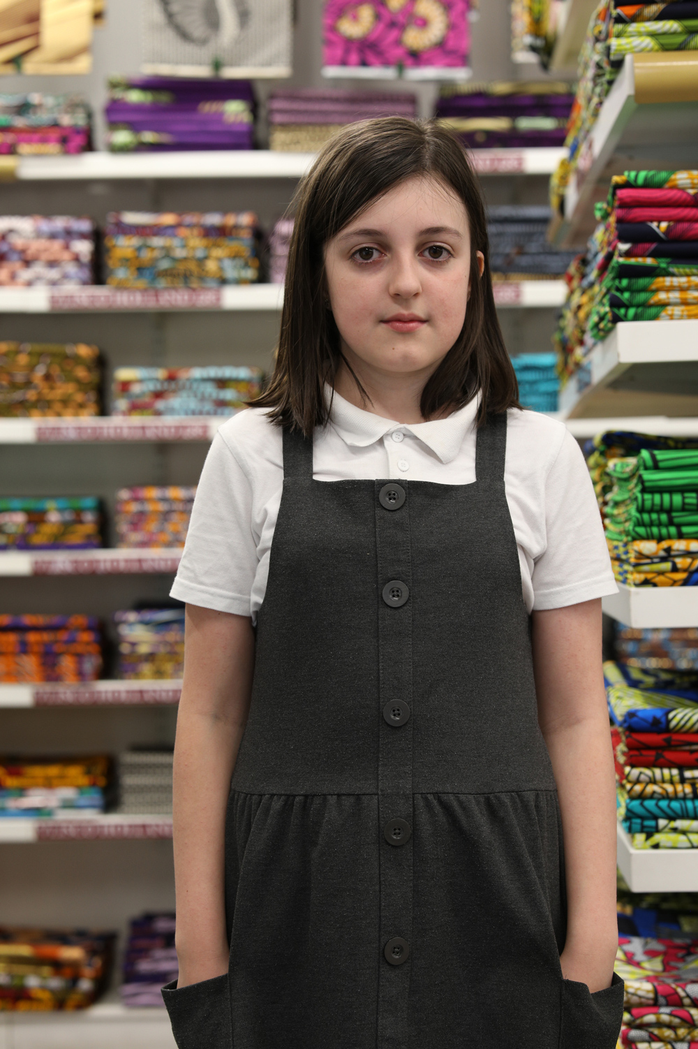 Portrait of a girl in school uniform standing in front of shelves of folded fabrics.