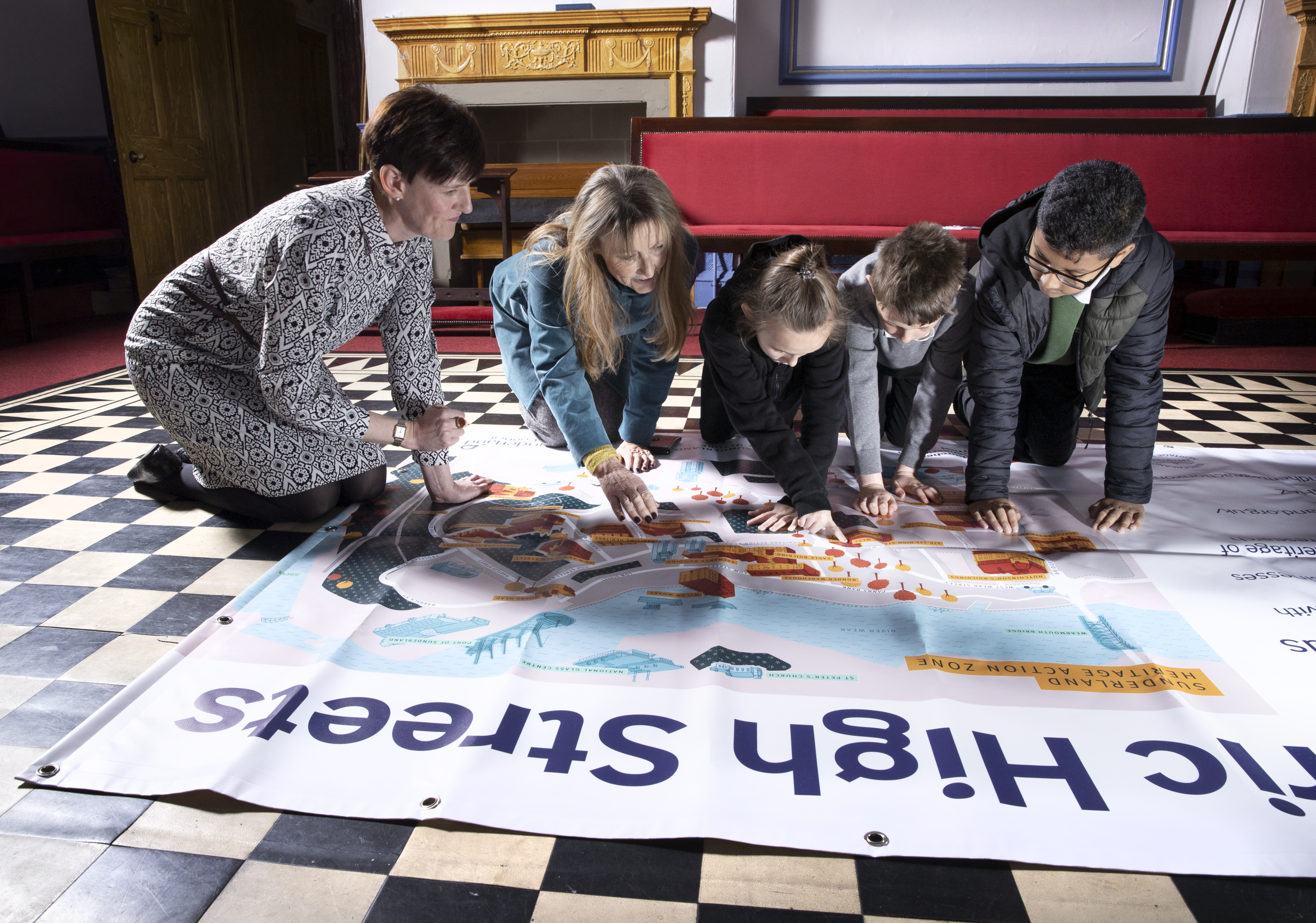 Three children and two adults looking at a banner map on an indoor floor.