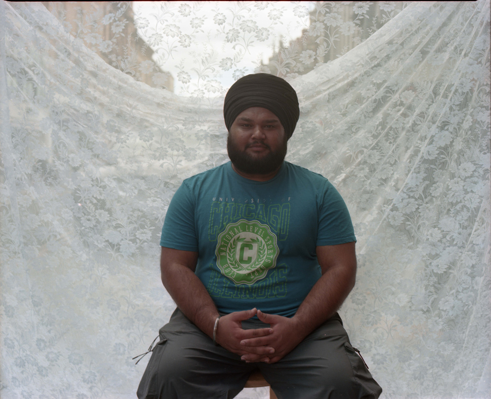 Portrait photo of a man against a backdrop of net curtain fabric.