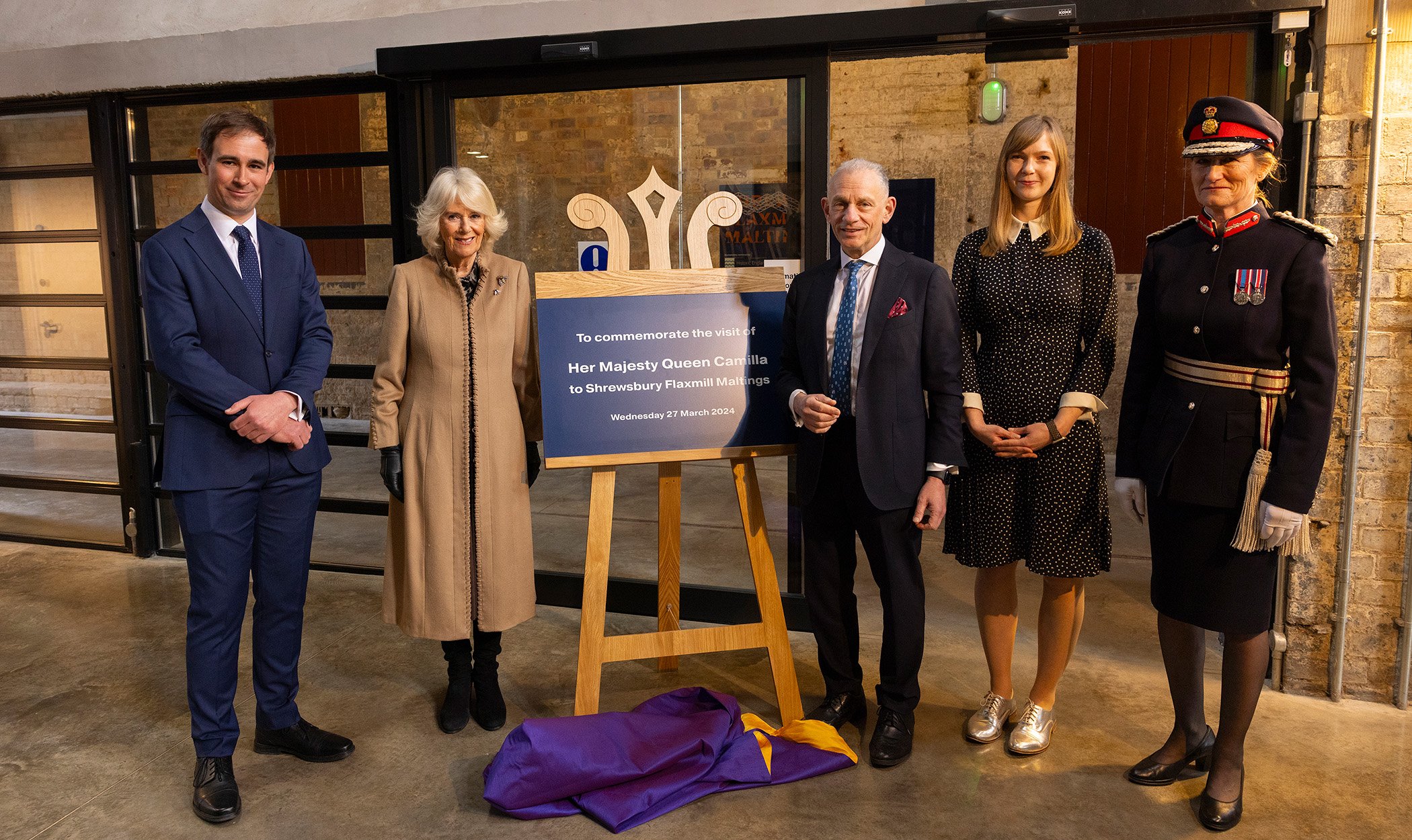 A photograph of five people stood next to a plaque being unveiled on a wooden easel