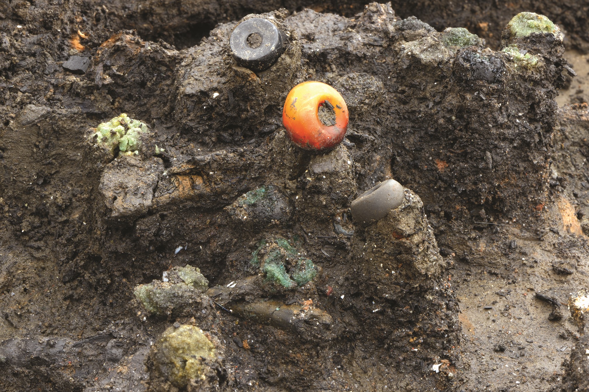 Two beads - one large orange bead and a small grey bead - seen in the ground at Must Farm