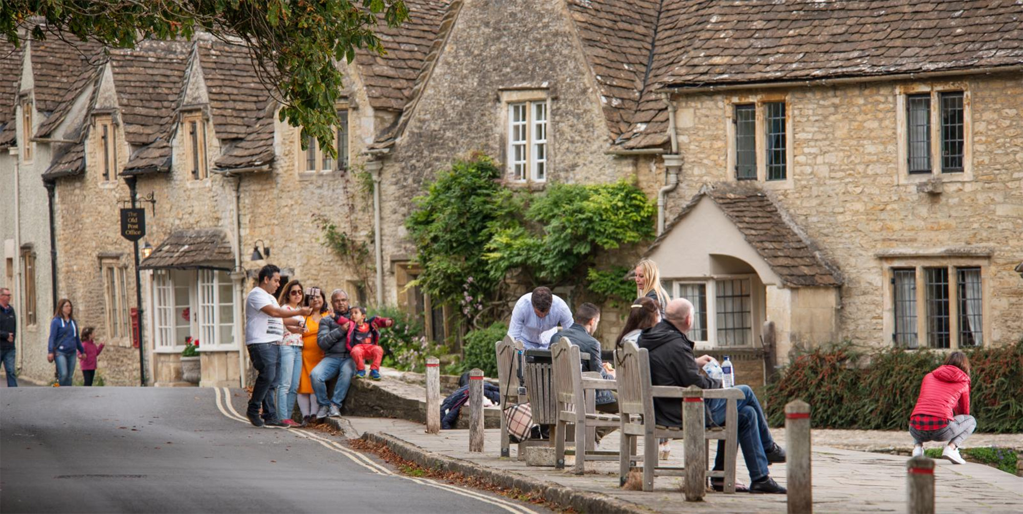 People sitting on benches with stone cottages in the background