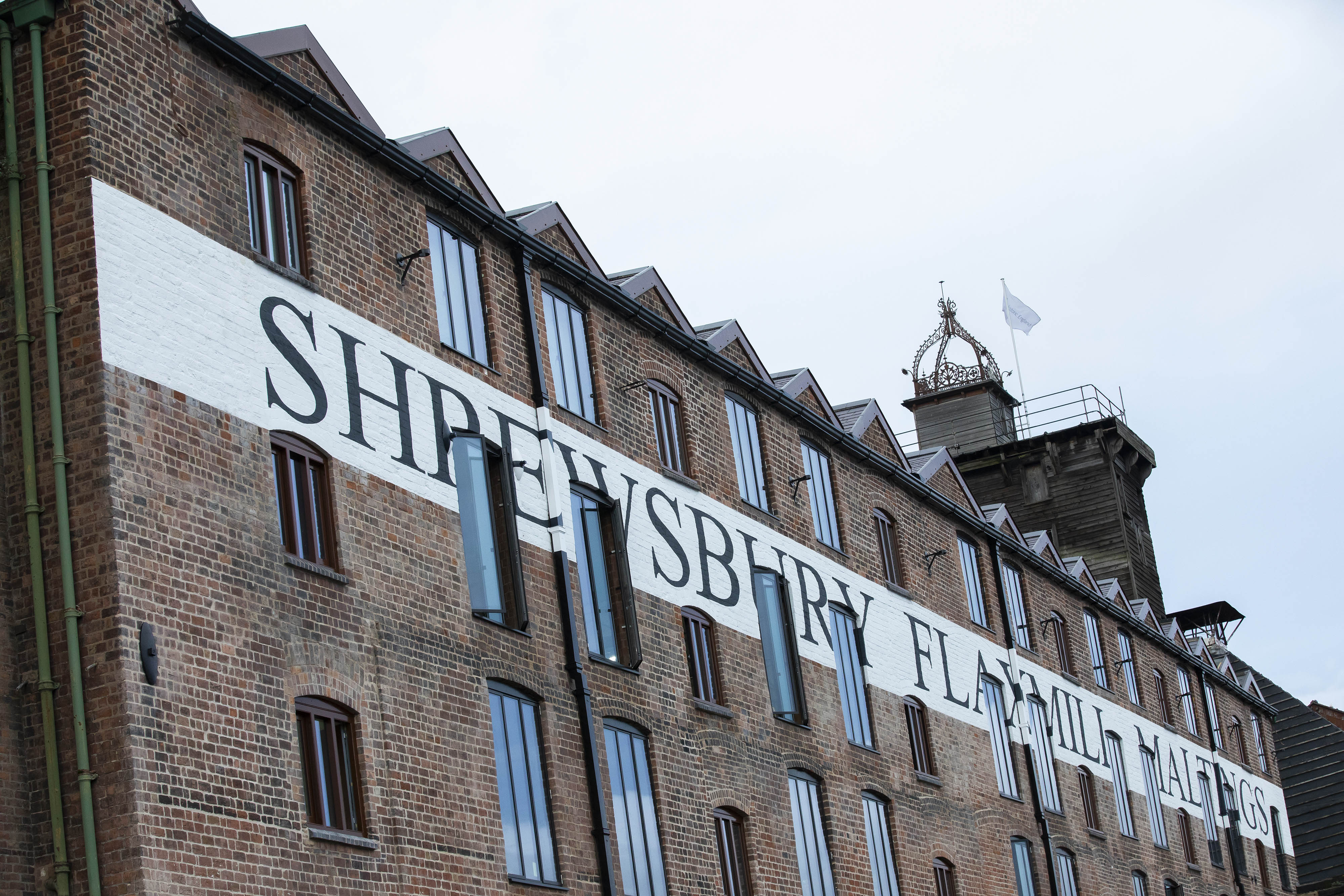 Sidelong view of mill building with the words 'Shrewsbury Flaxmill Maltings' painted in black on a white band on the building