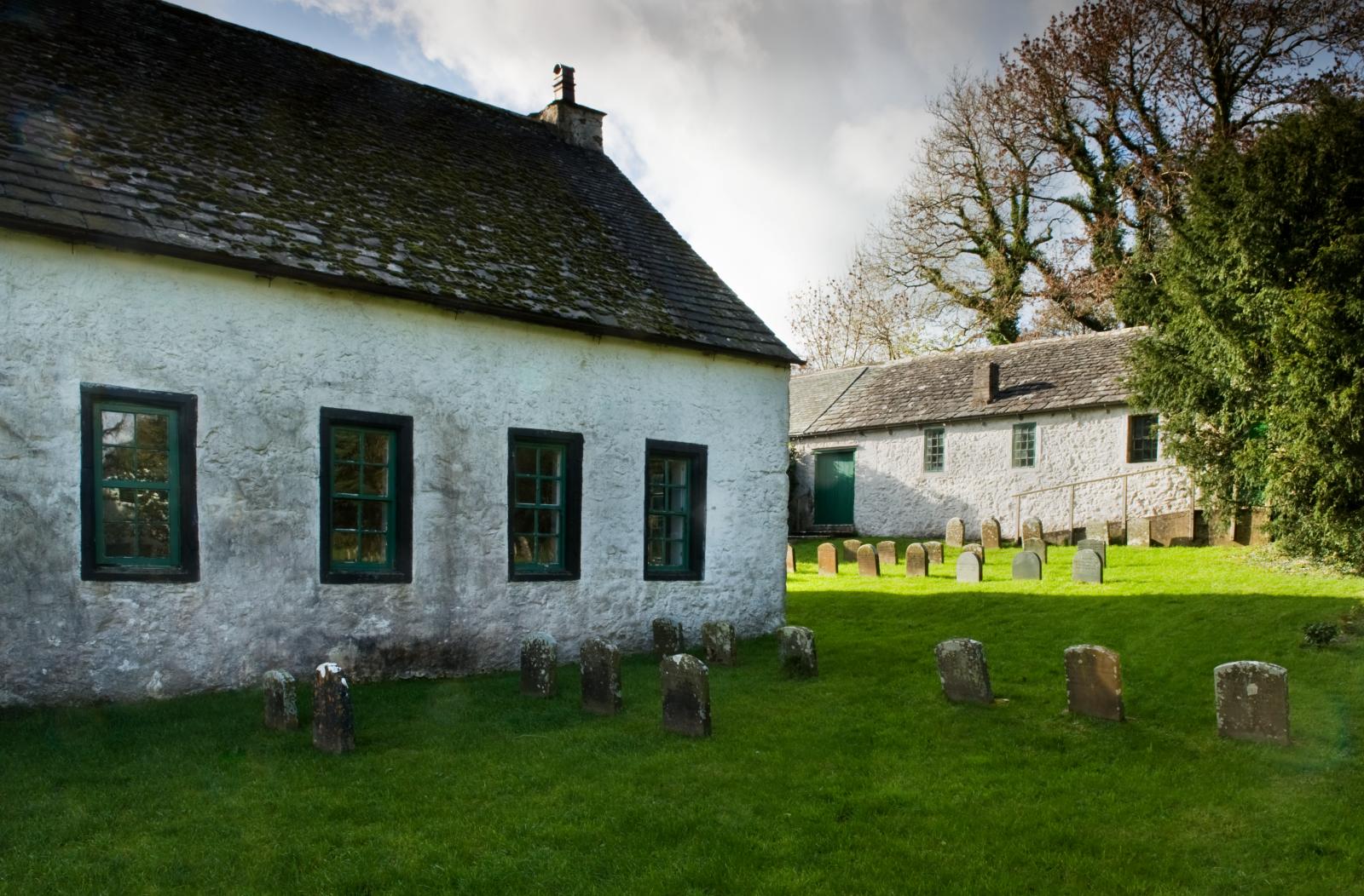Exterior shot of Pardshaw meeting house with white walls and green window frames in a burial ground.
