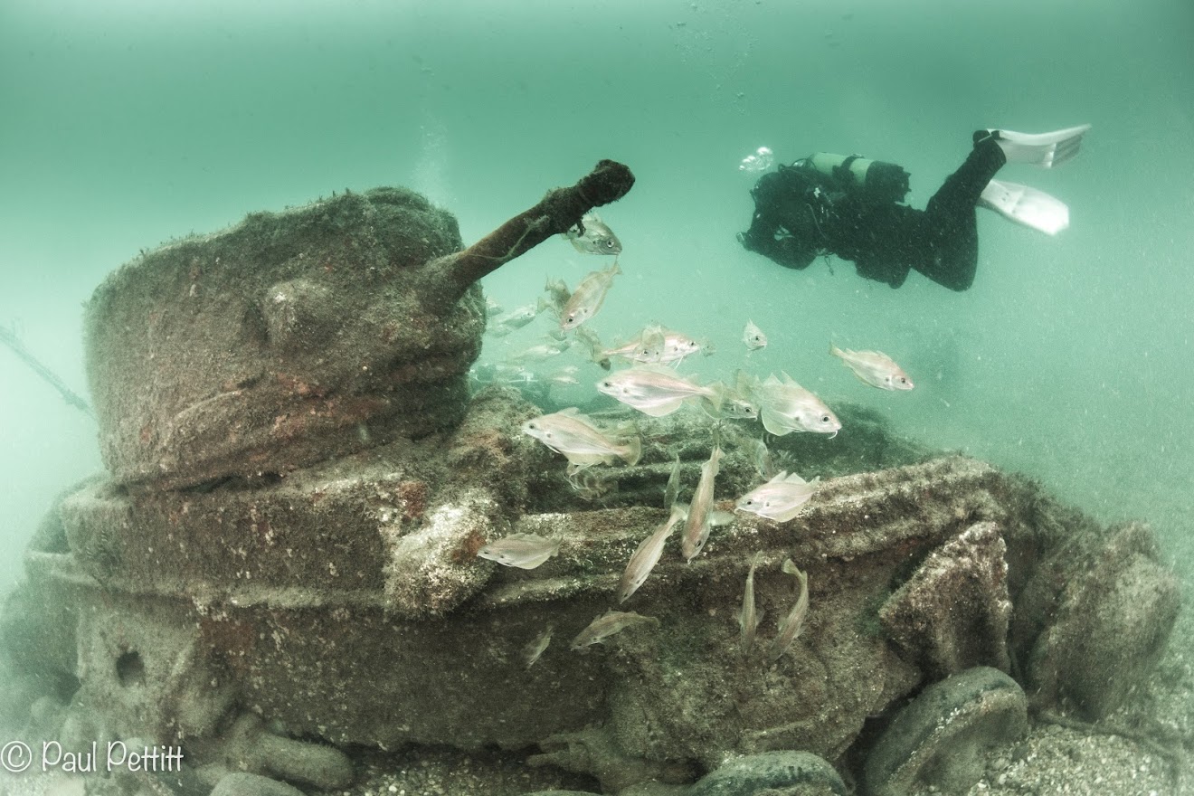 The submerged remains of a tank being recorded by a diver.