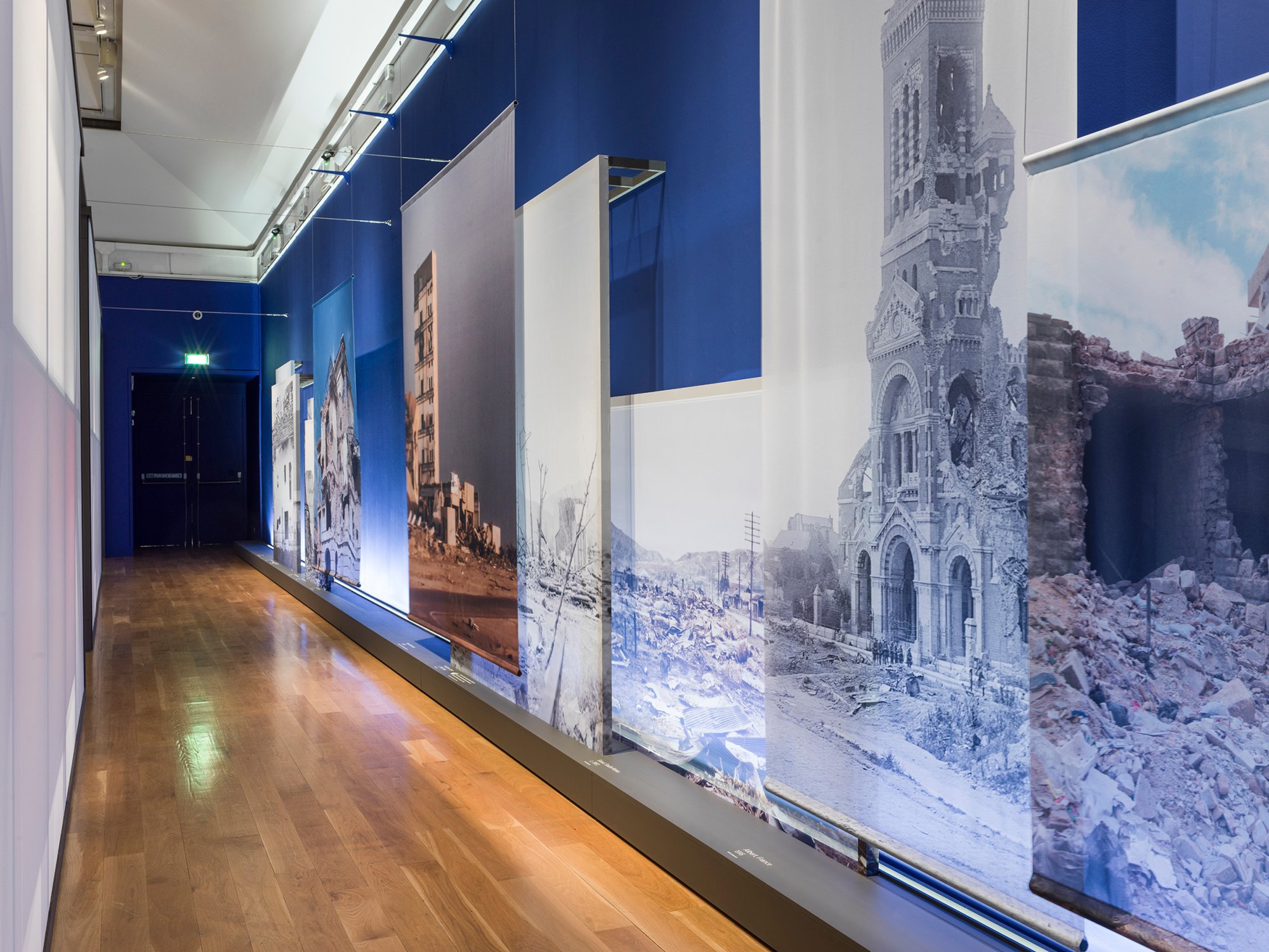 Large prints of bomb damaged buildings hang along the wall of a corridor at Historic England's What Remains exhibition at the Imperial War Museum.