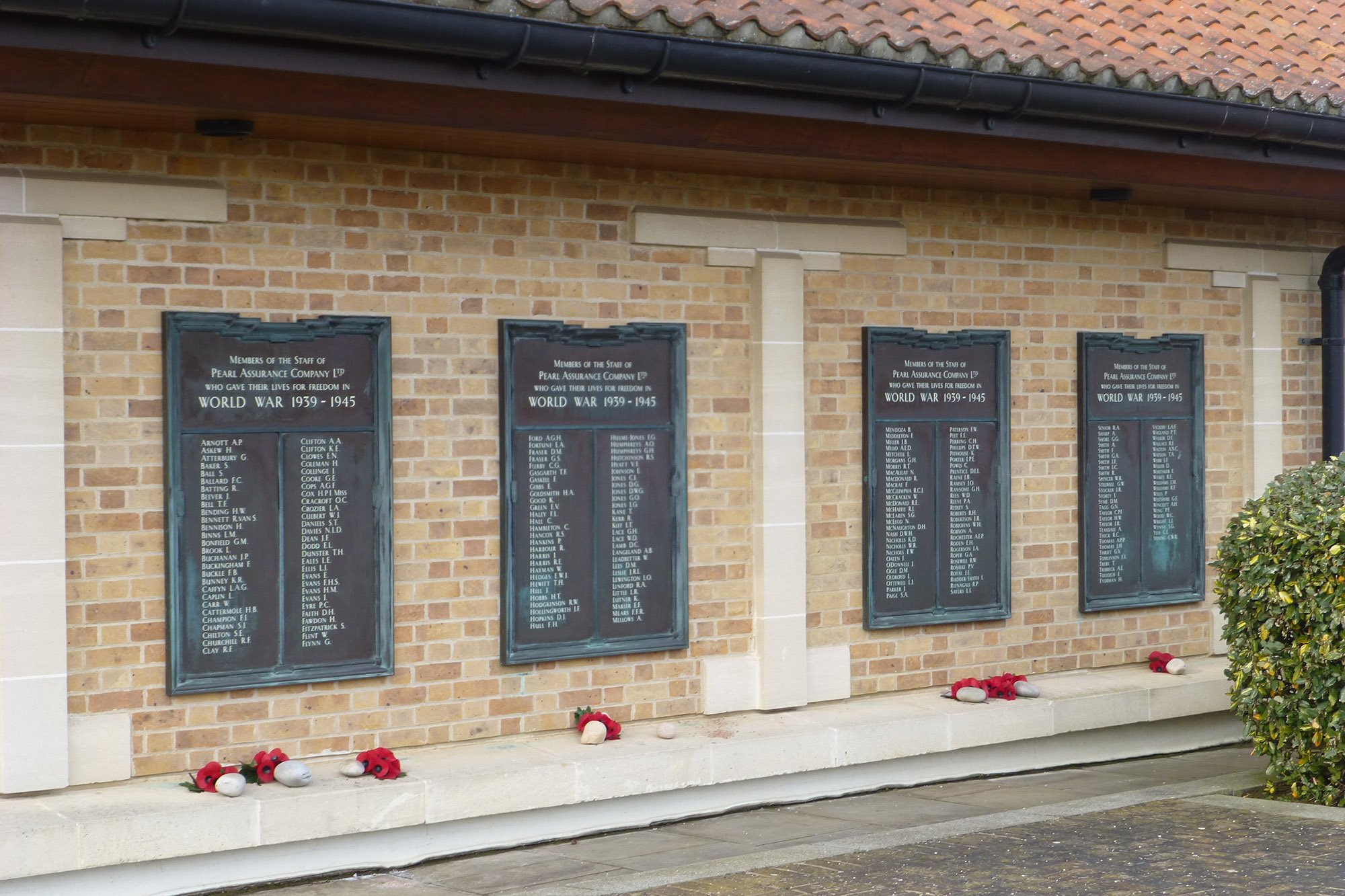 Four bronze plaques set in a brick wall with poppy wreaths placed underneath them.
