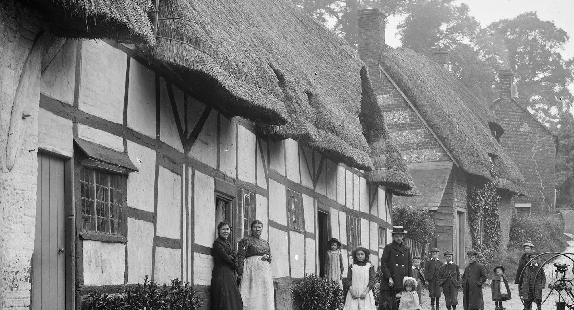 Exterior view of women and children posing outside a thatched cottage