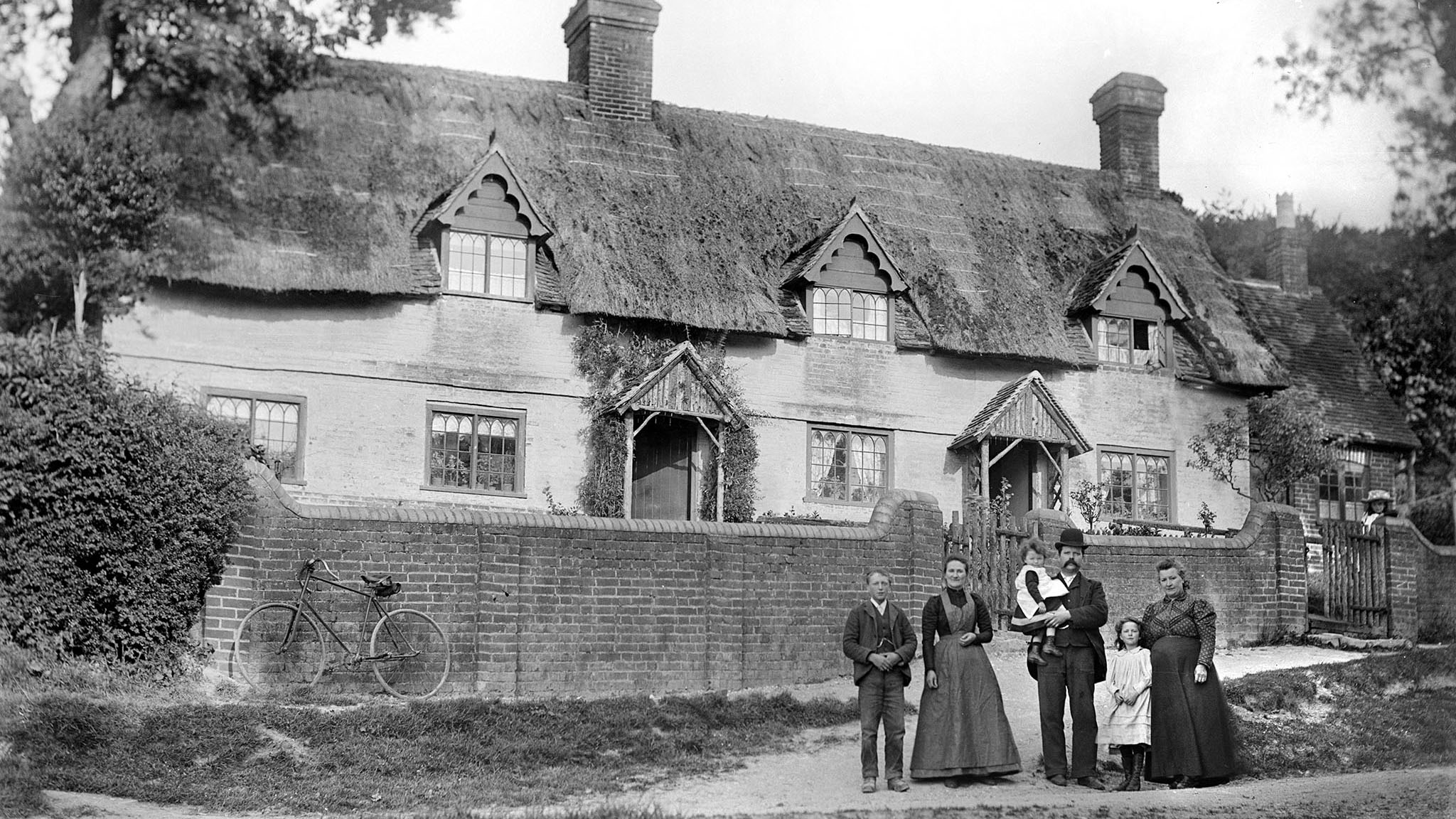 Row of unidentified brick and thatch cottages with family group in front