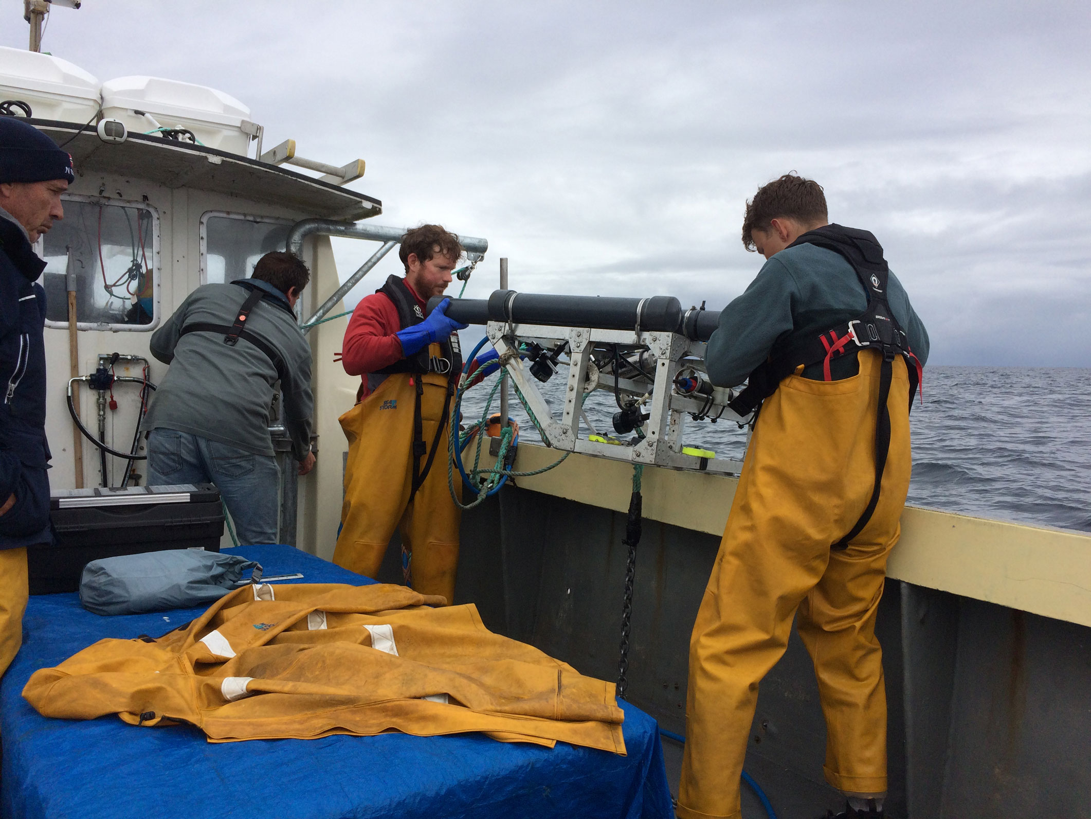 Survey crew members deploying an Underwater Towed Vehicle over the side of a fishing boat.