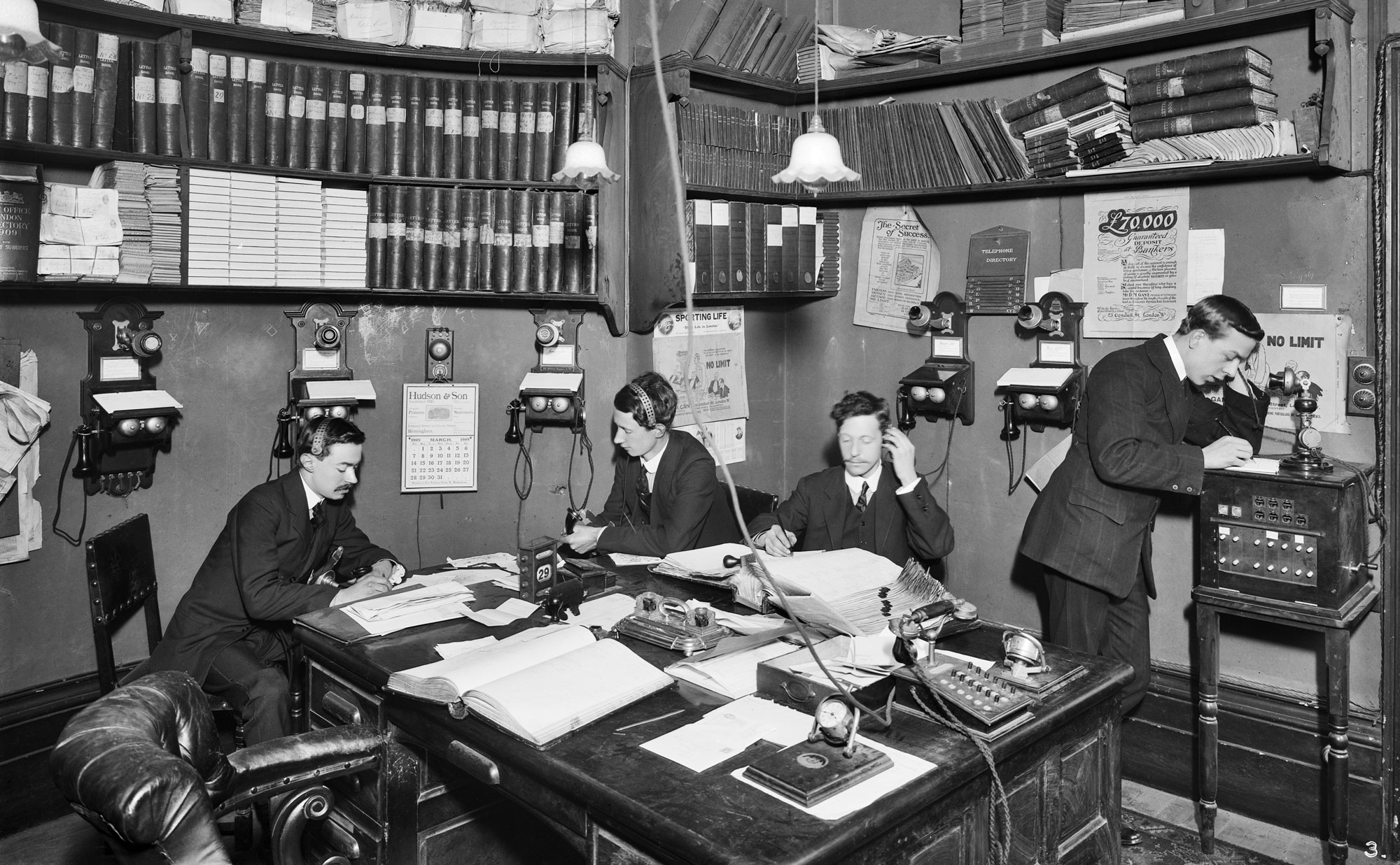 A black and white photo of the interior of a crowded office in 1909.