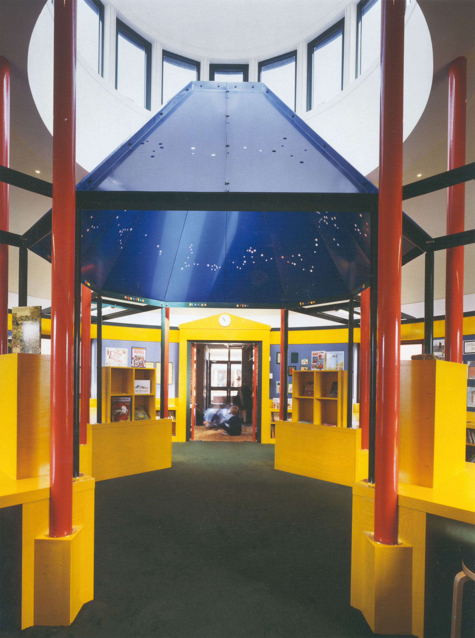 The interior of the Bishop Wilson Memorial Library shows the bright red columns, blue painted canopy and yellow door frames, shelves and wall coverings.