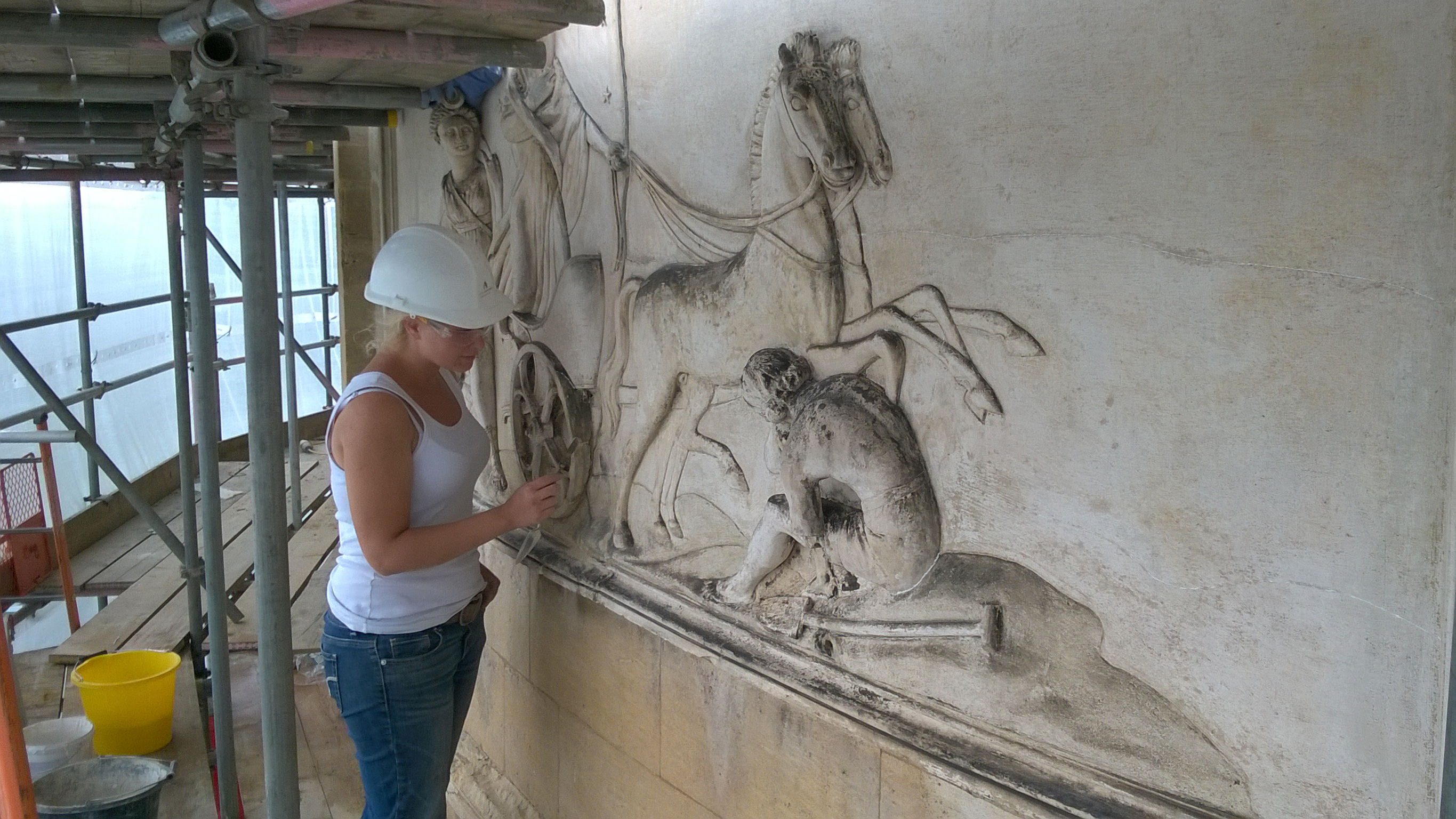 Woman wearing hard hat working on a stone carving under scaffolding