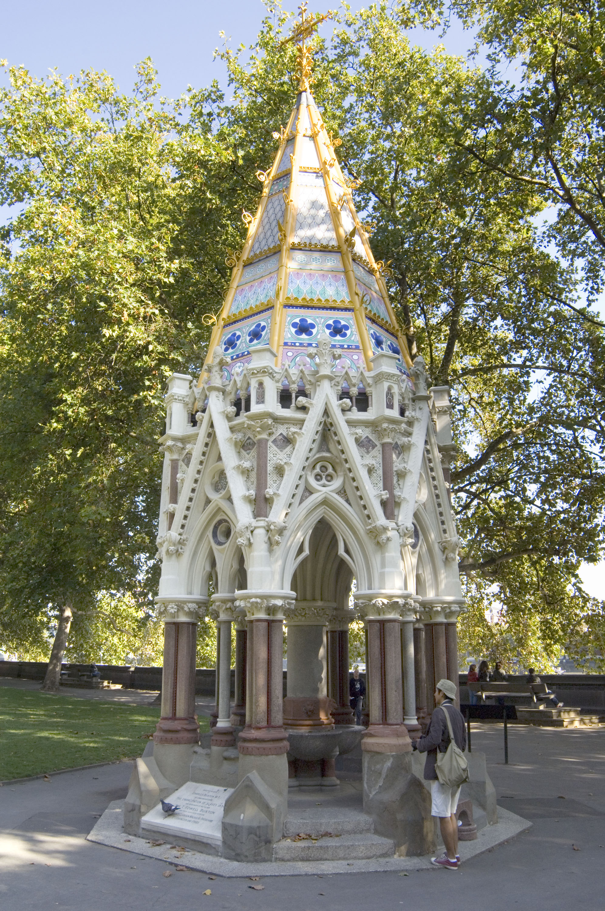 Elaborate Victorian Gothic pavilion, octagonal with a spire roof. Below, a stone arcade with pointed trefoil arches on red granite shafts. Above, the roof covered with bright enamelled decoration – pink, white, blue, green and yellow.