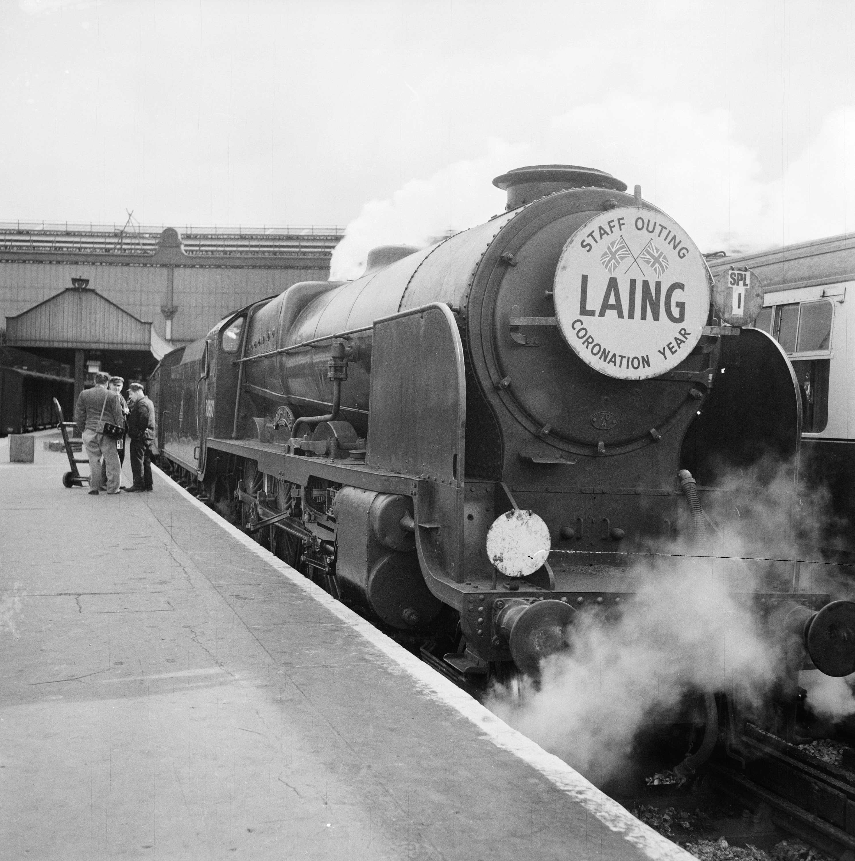 Steam train in station with a placard on the front which reads, 'LAING -  STAFF OUTING - CORONATION YEAR'