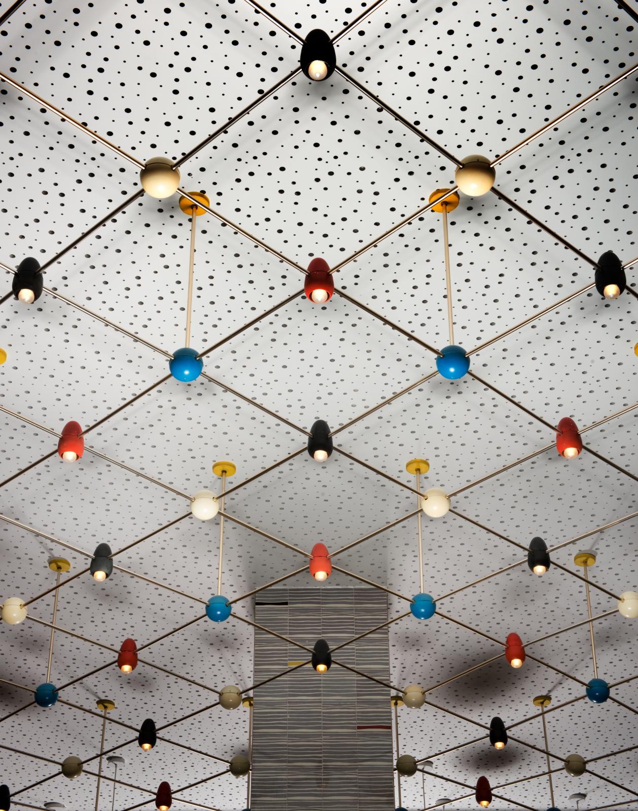 white lights with multi coloured lampshades suspended from a ceiling. The ceiling is white with dark speckles and square patterns