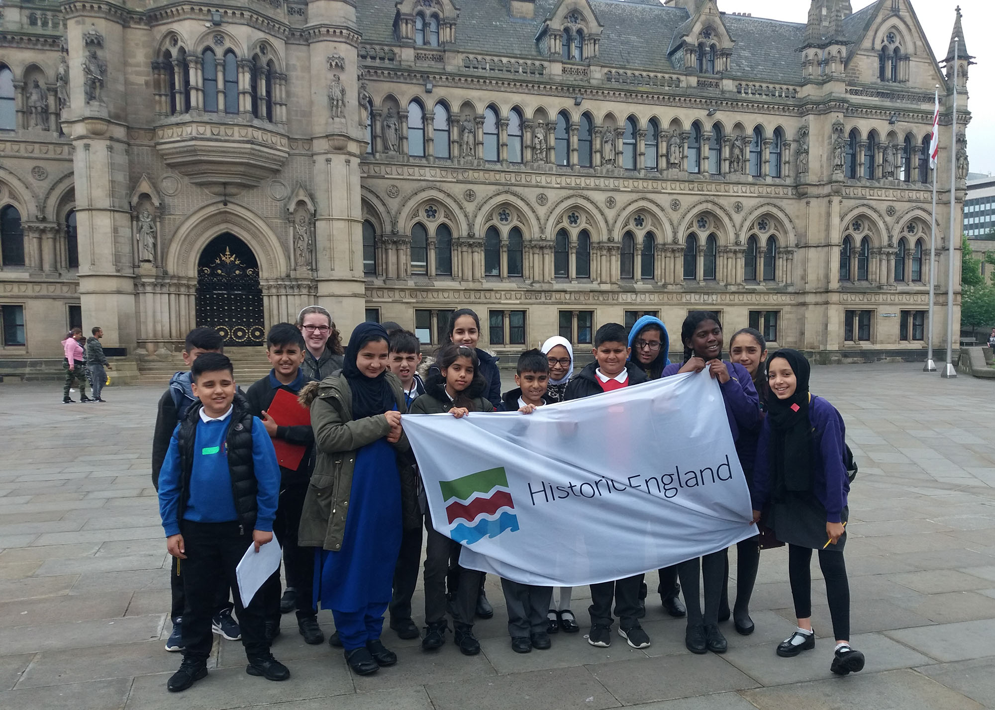 Pupils outside Bradford City Hall holding a banner with the Historic England logo on it.
