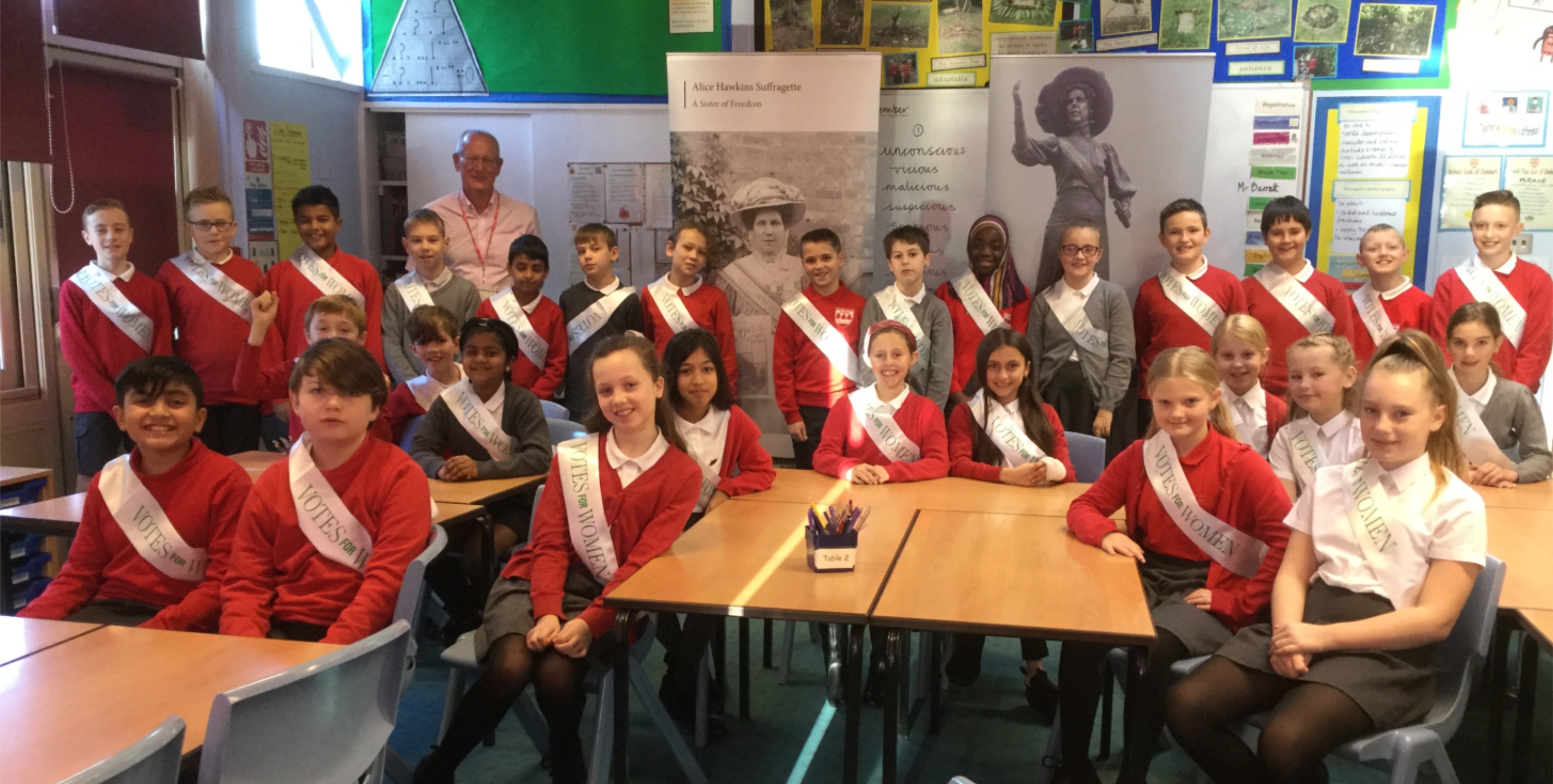 Group photo of pupils in a classroom wearing school uniform and 'votes for women' sashes