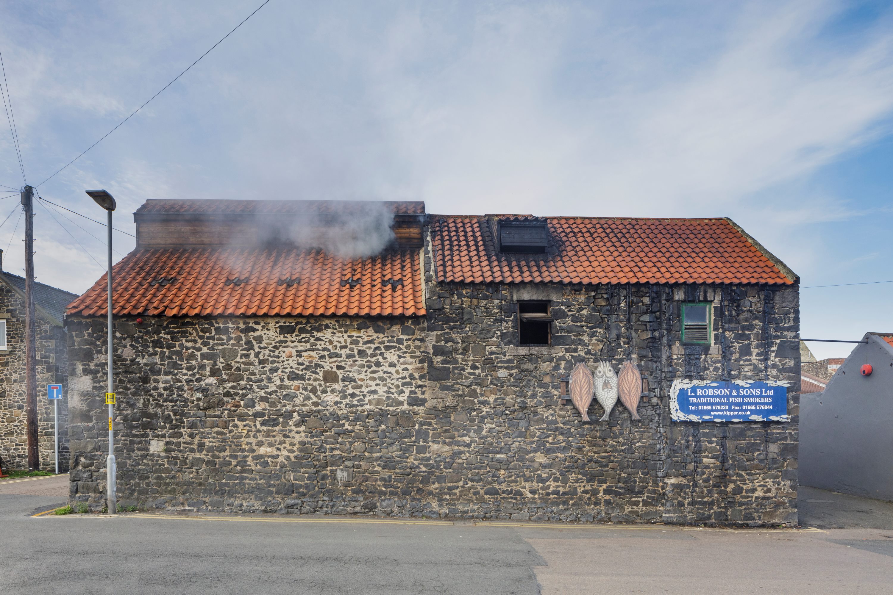 A stone building next to a road with smoke coming out of the roof.