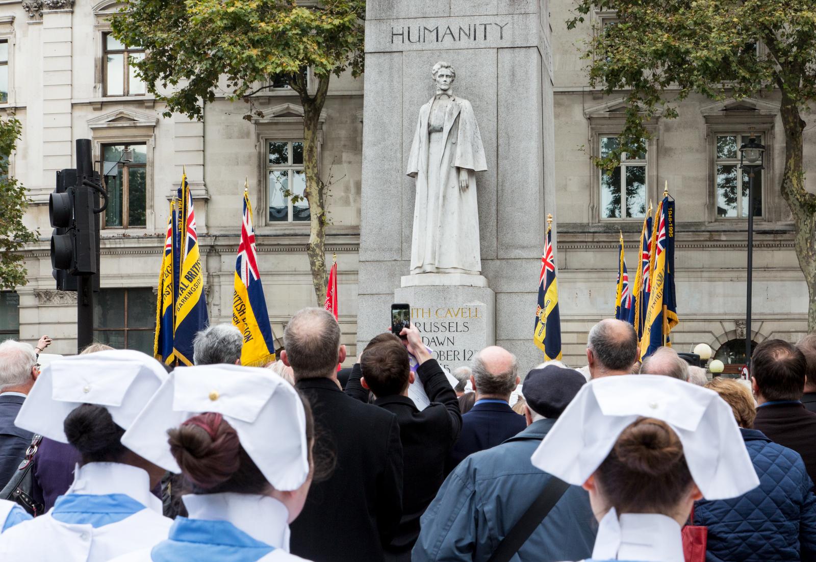 Crowds gathered in front of Edith Cavell memorial. Some are nurses in uniform.