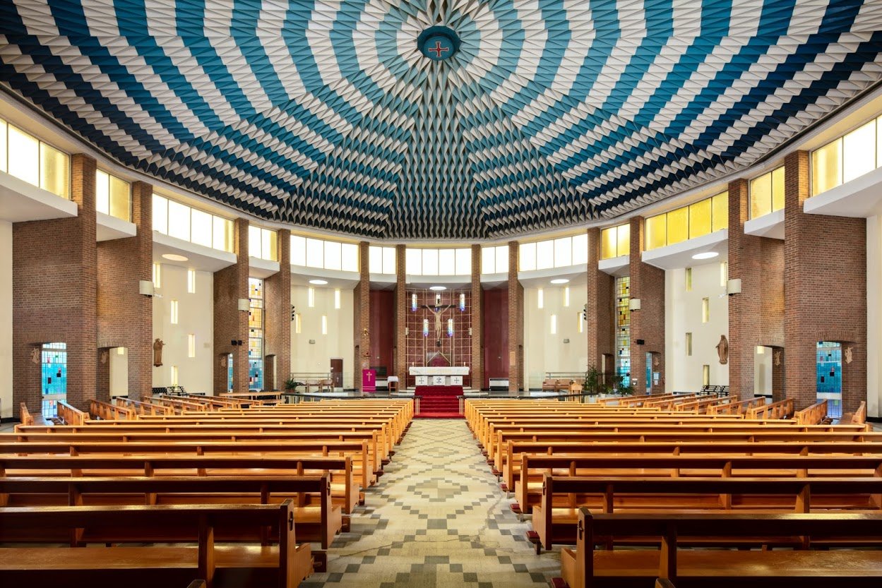 A beautiful blue and white fan shaped ceiling dominates the circular interior of St Mary's Dunstable. Also seen are long wooden pews, an ornate mosaic flooring, simple pillars and altar.